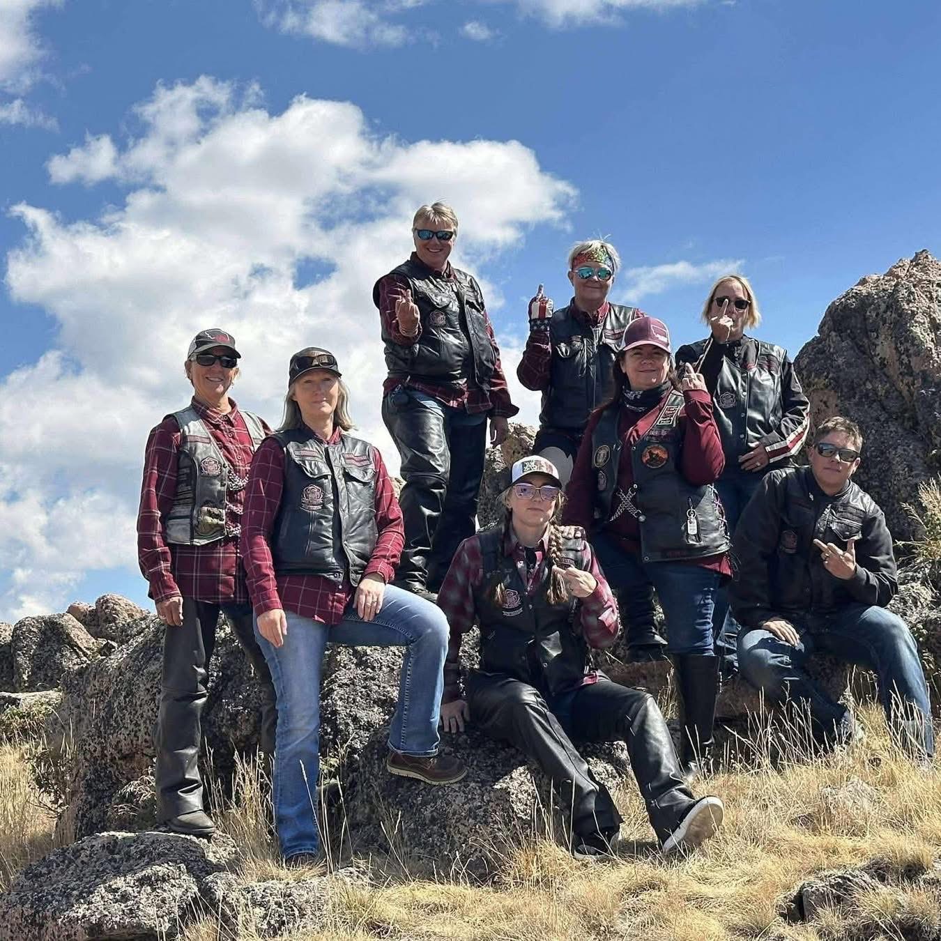 Group of eight people outdoors on rocks, some sitting and some standing, with a blue sky and clouds in background.