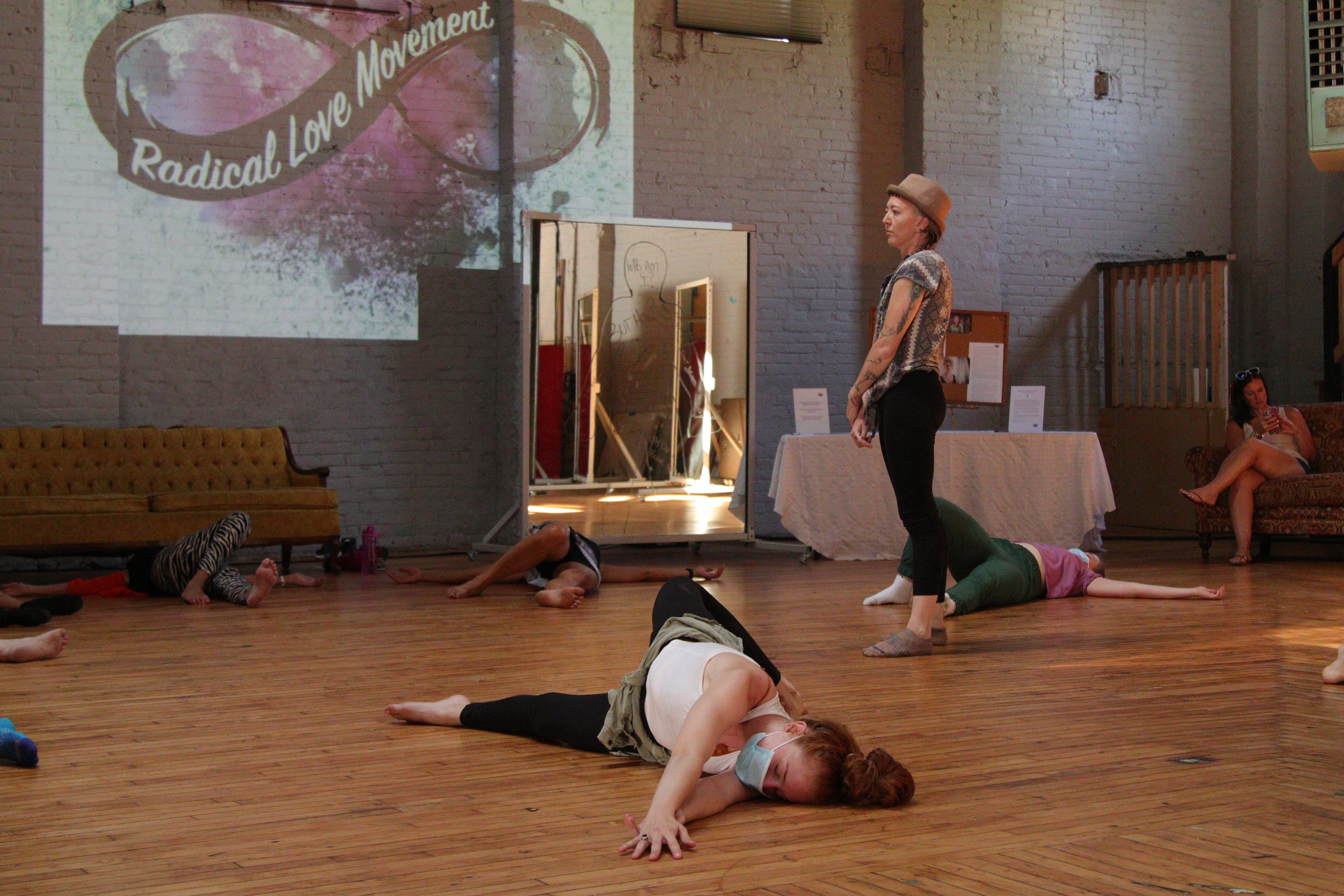 Group of people practicing dance or movement in a studio with a wooden floor and a projection on the wall.
