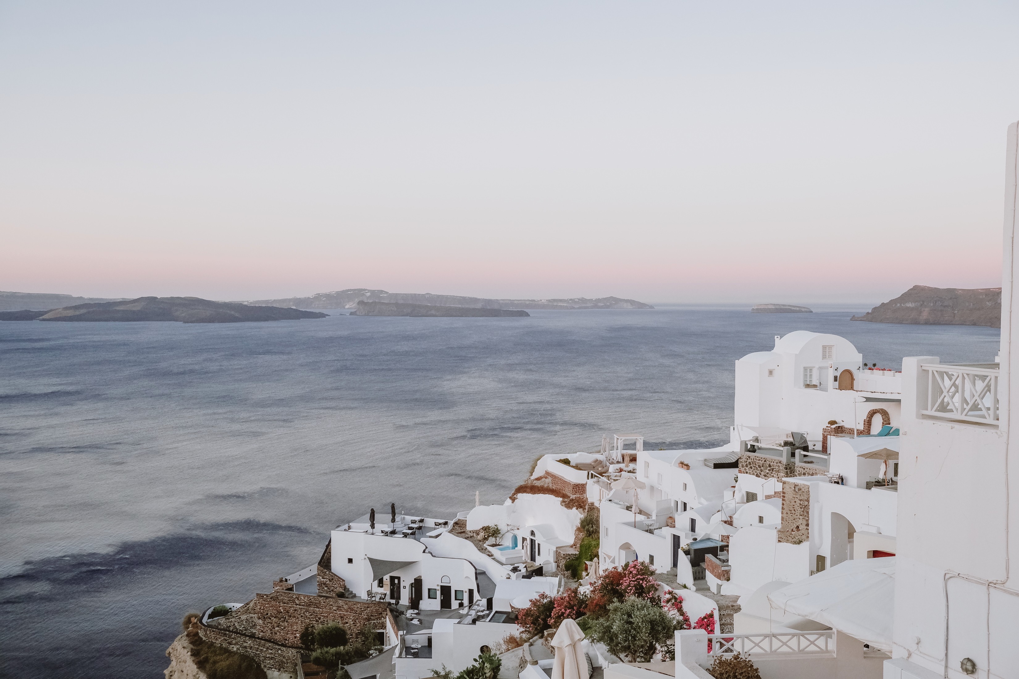Coastal scene with white buildings on a hillside overlooking water and distant landforms, clear sky, calm atmosphere.