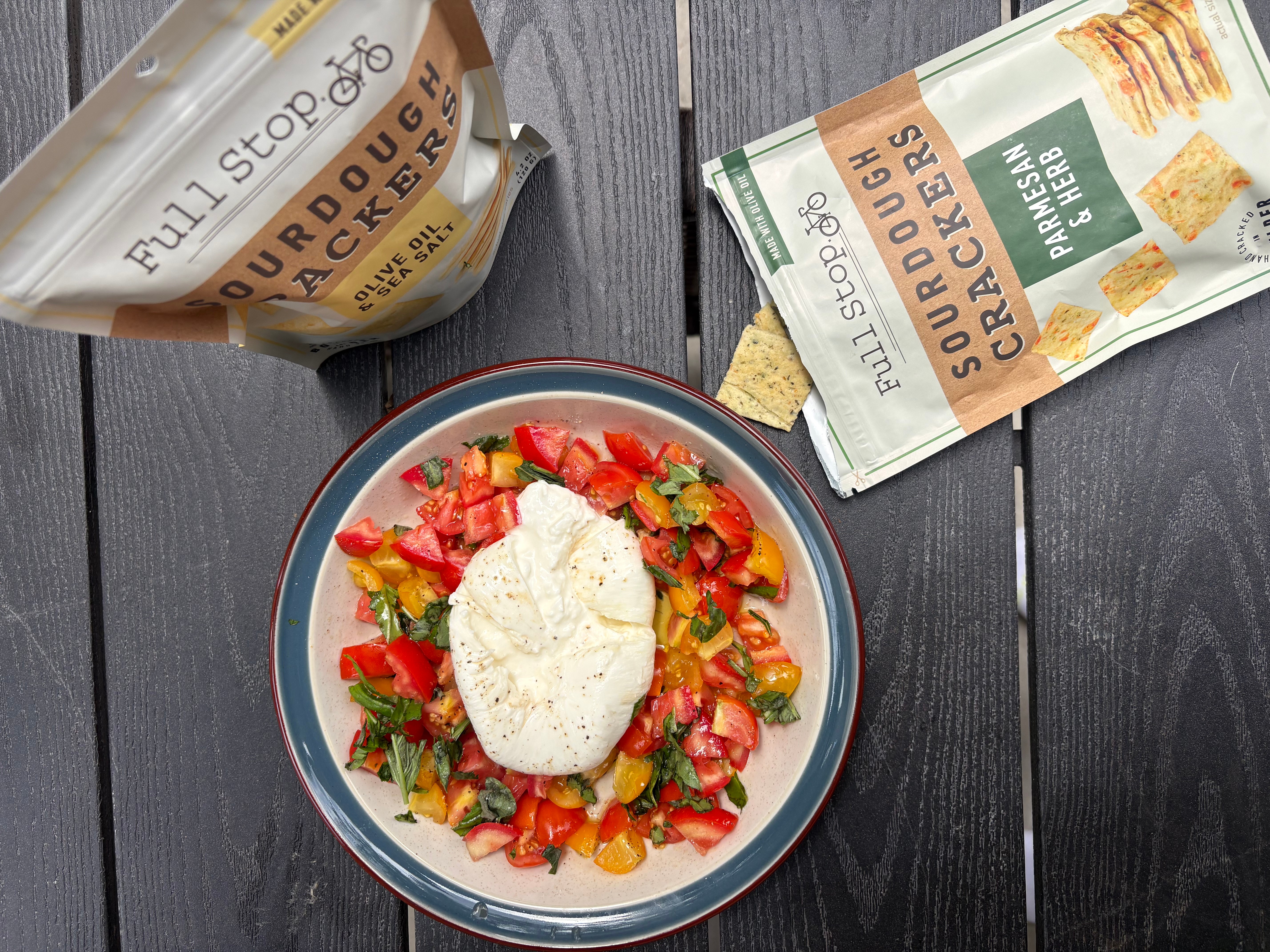 Bowl with salad topped with a dollop of white dressing, surrounded by snack packets on a dark wooden surface.