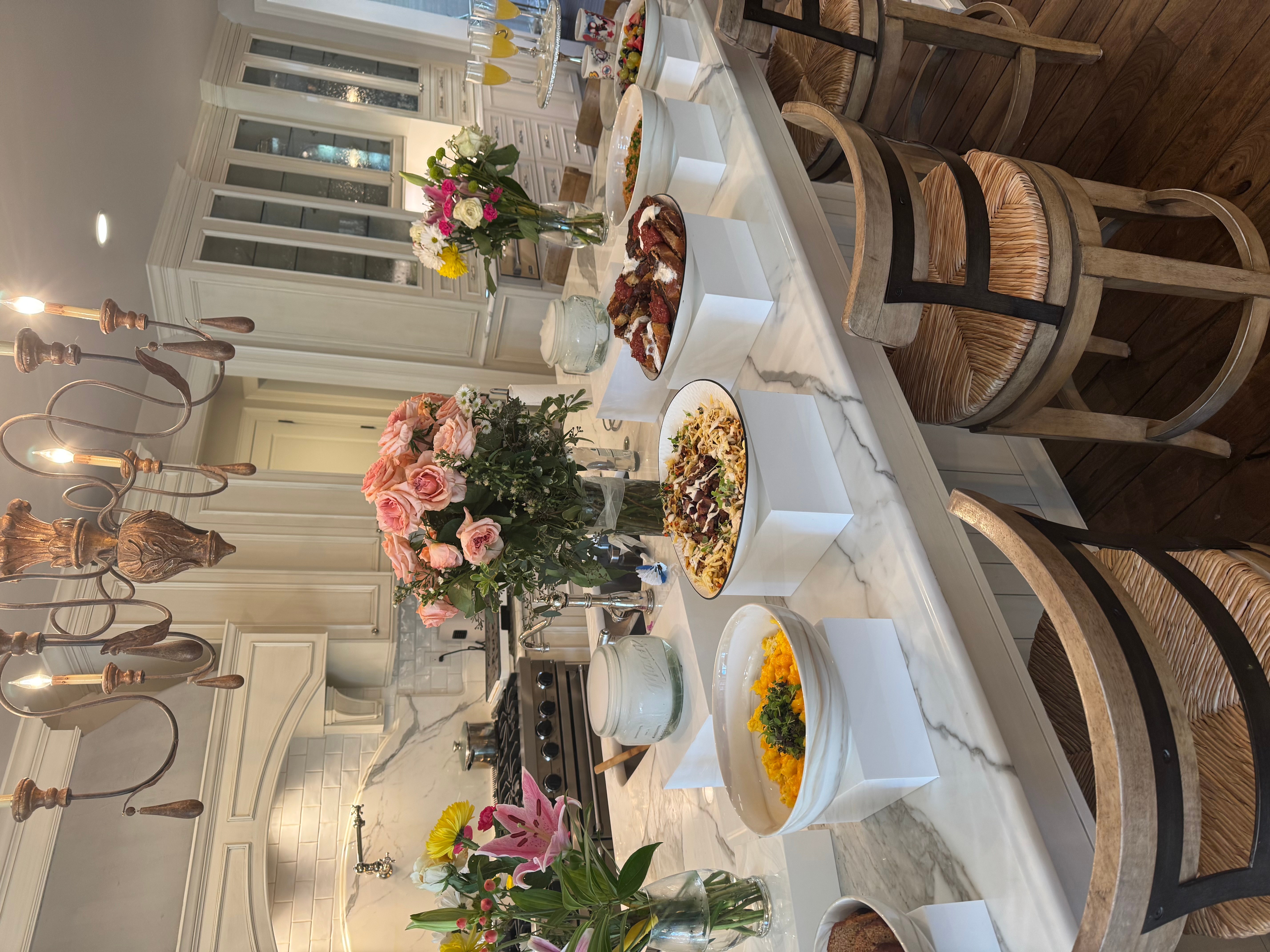 Dining table with flowers, food, and drinks in a bright room, with chairs around the table.