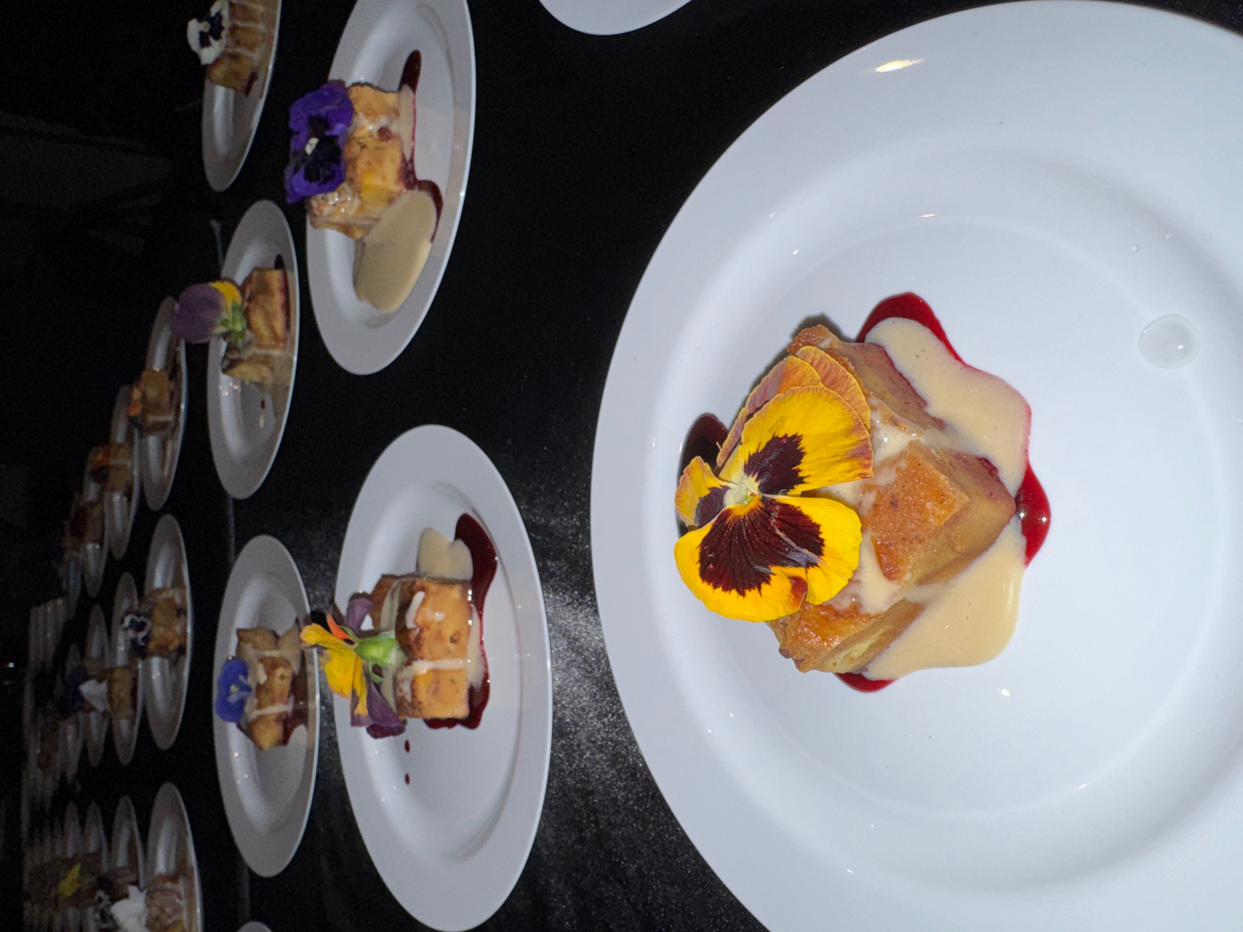 A dessert with a flower garnish on a white plate, with other desserts on similar plates in the background.