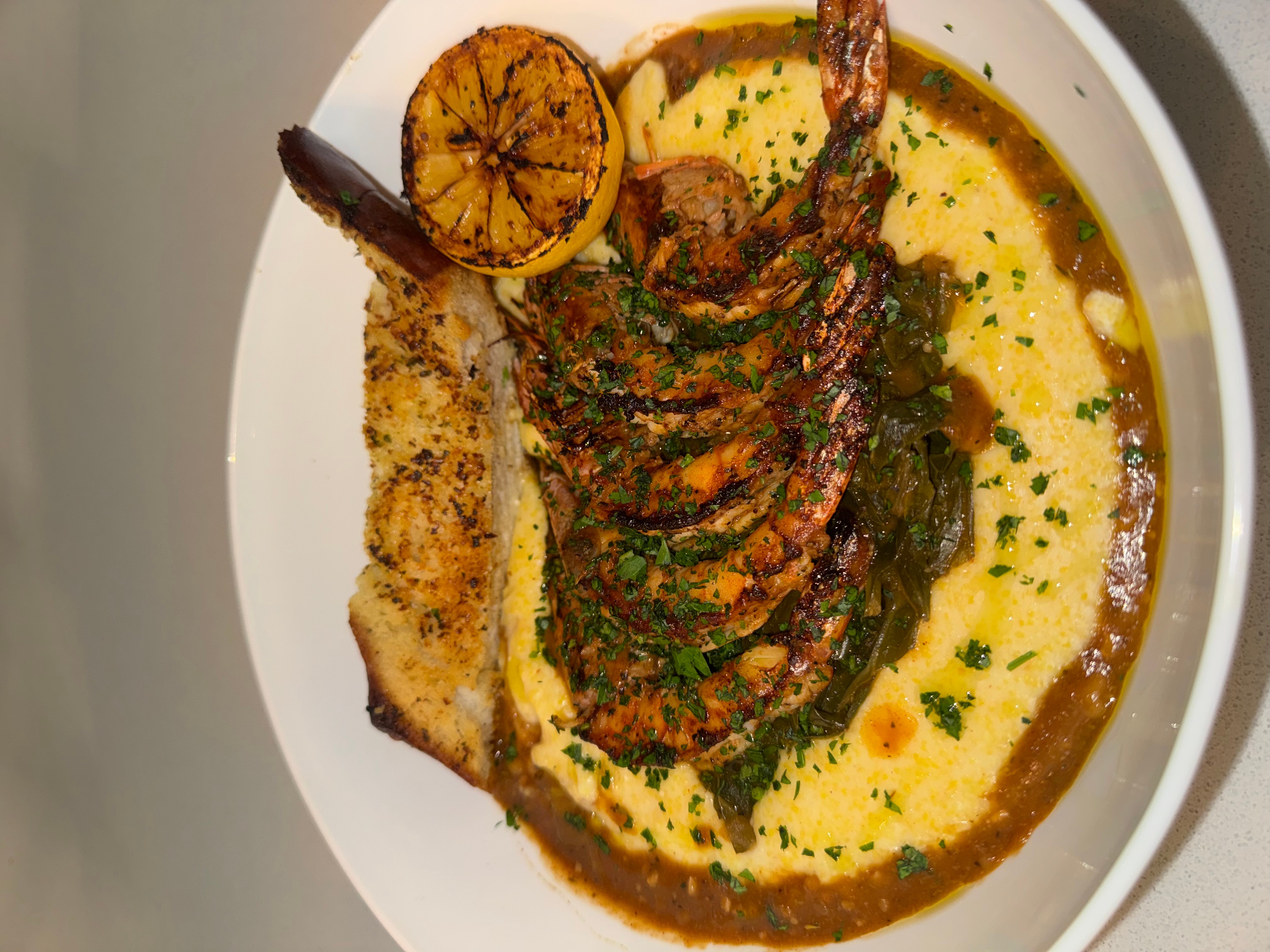 Grilled lobster tail with lemon, served on a bed of creamy sauce, garnished with herbs.