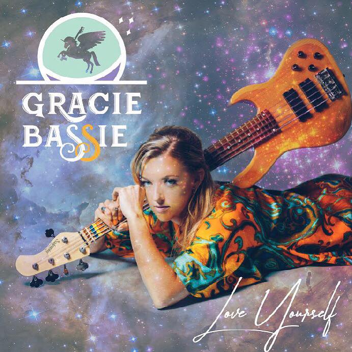 Woman lying on colorful fabric with guitar and a guitar-shaped object against a starry background, promoting Gracie Bassie, with text and logo.