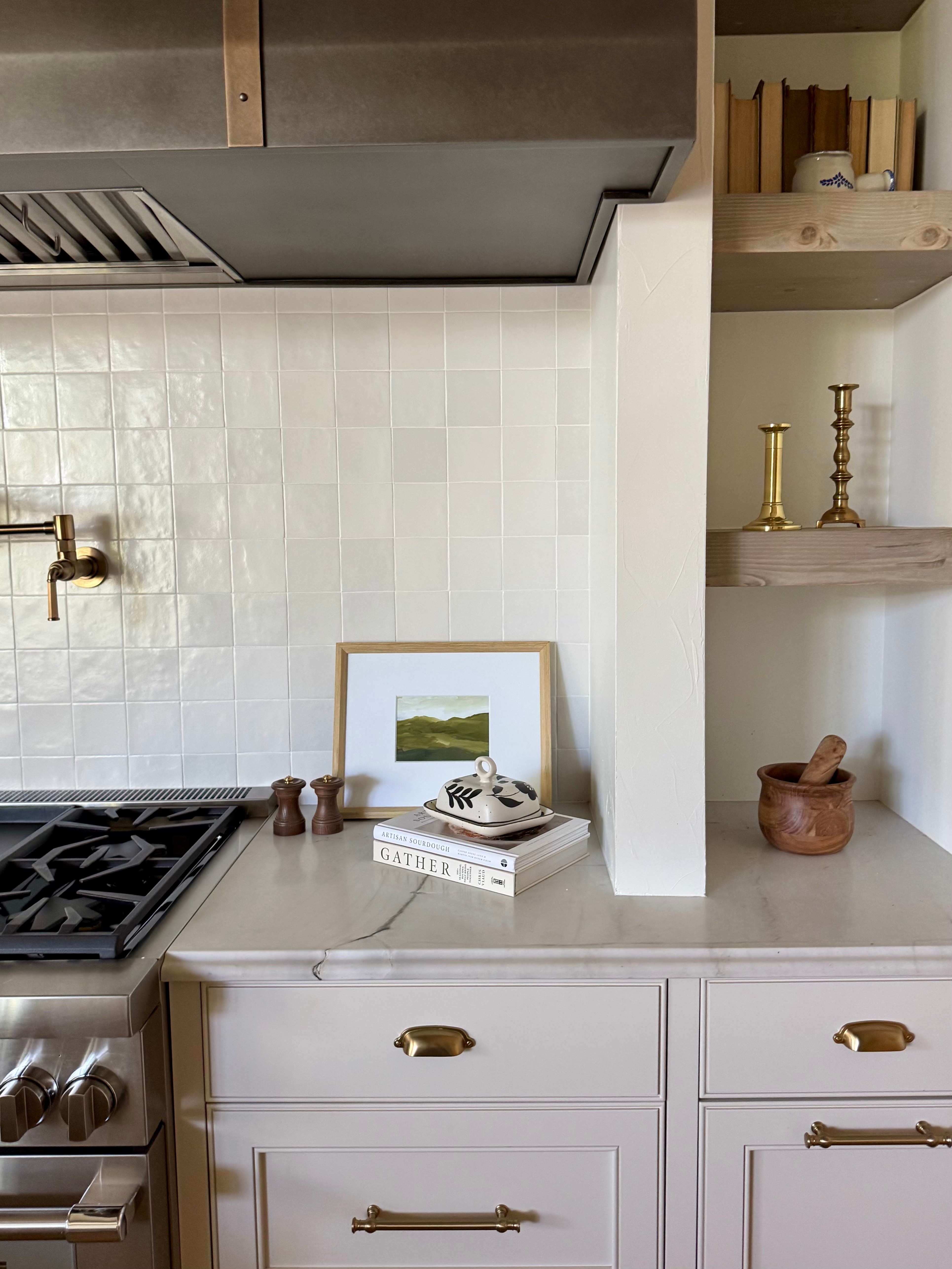Kitchen counter with a framed picture, books, and decorative items, including a mortar and pestle, against a white tiled wall.