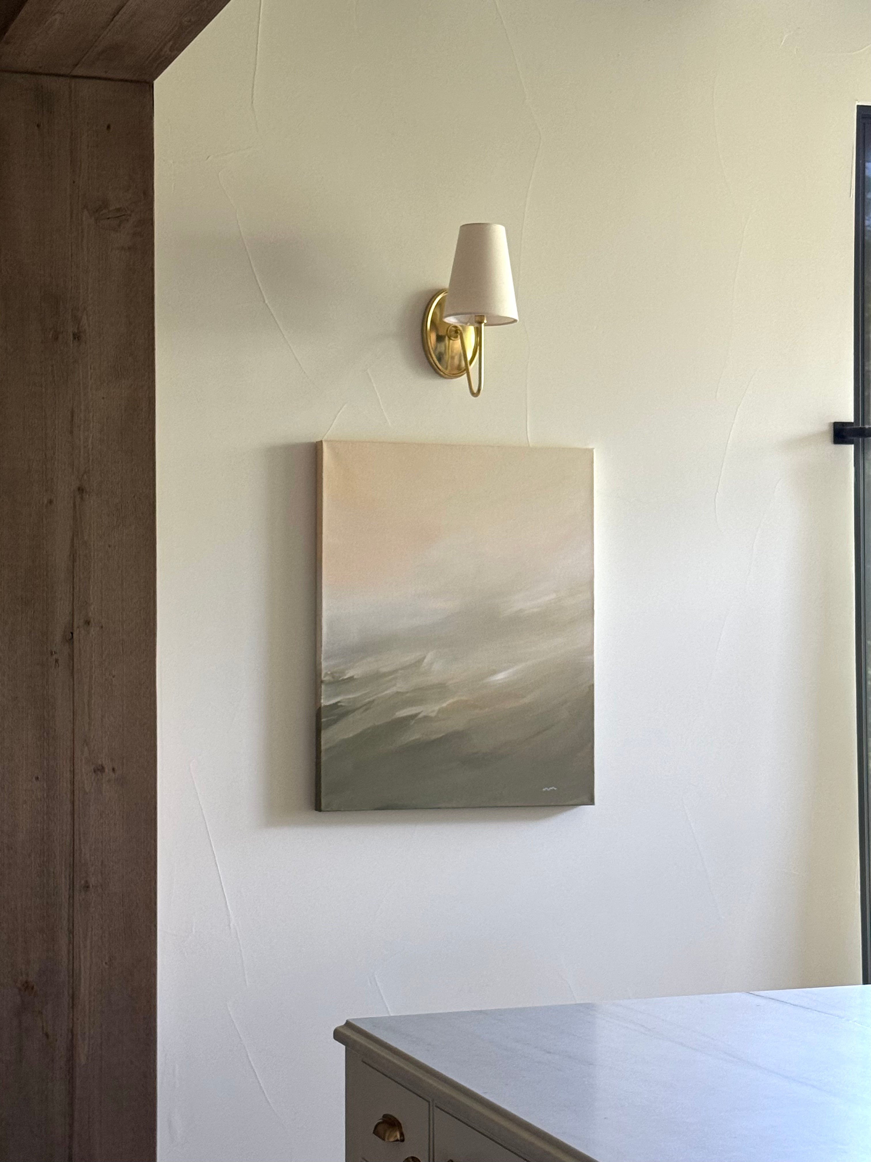 Wall with a painting and a wall-mounted lamp, part of a room interior, with a table in the foreground.