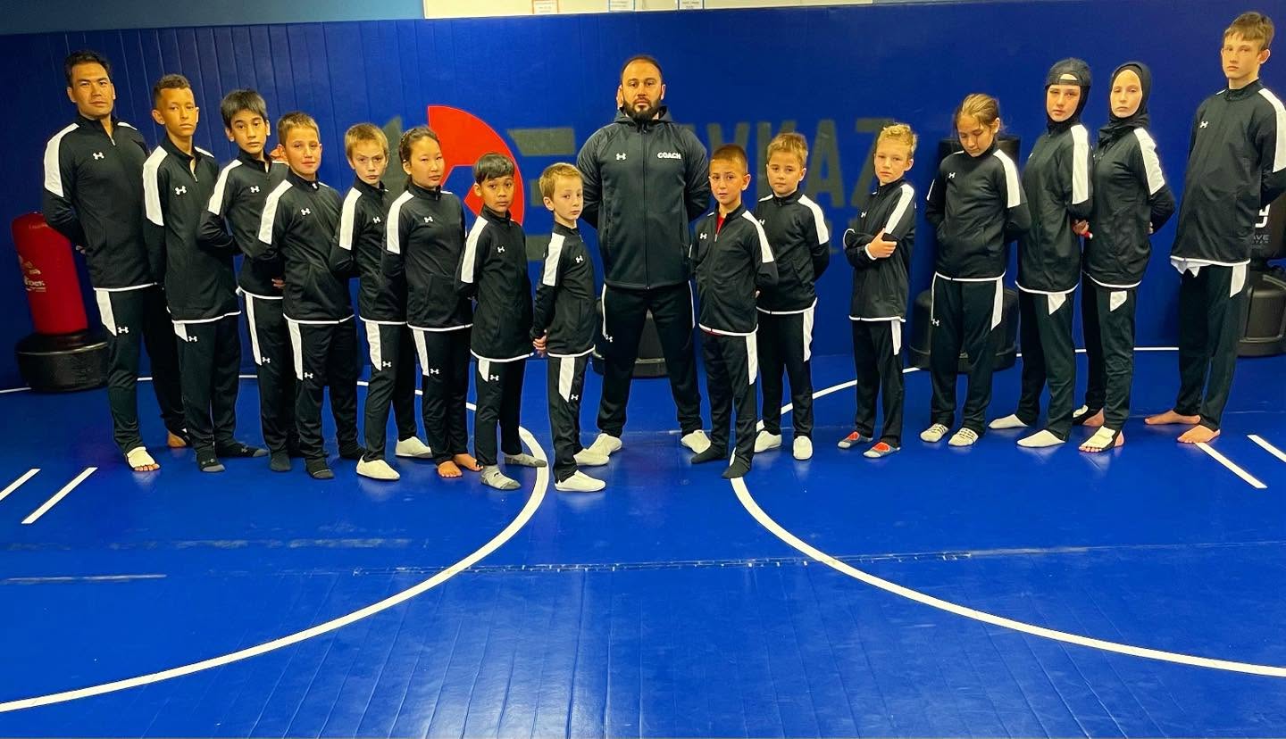 Group of children and adults in sports uniforms standing on a blue indoor court, facing forward.