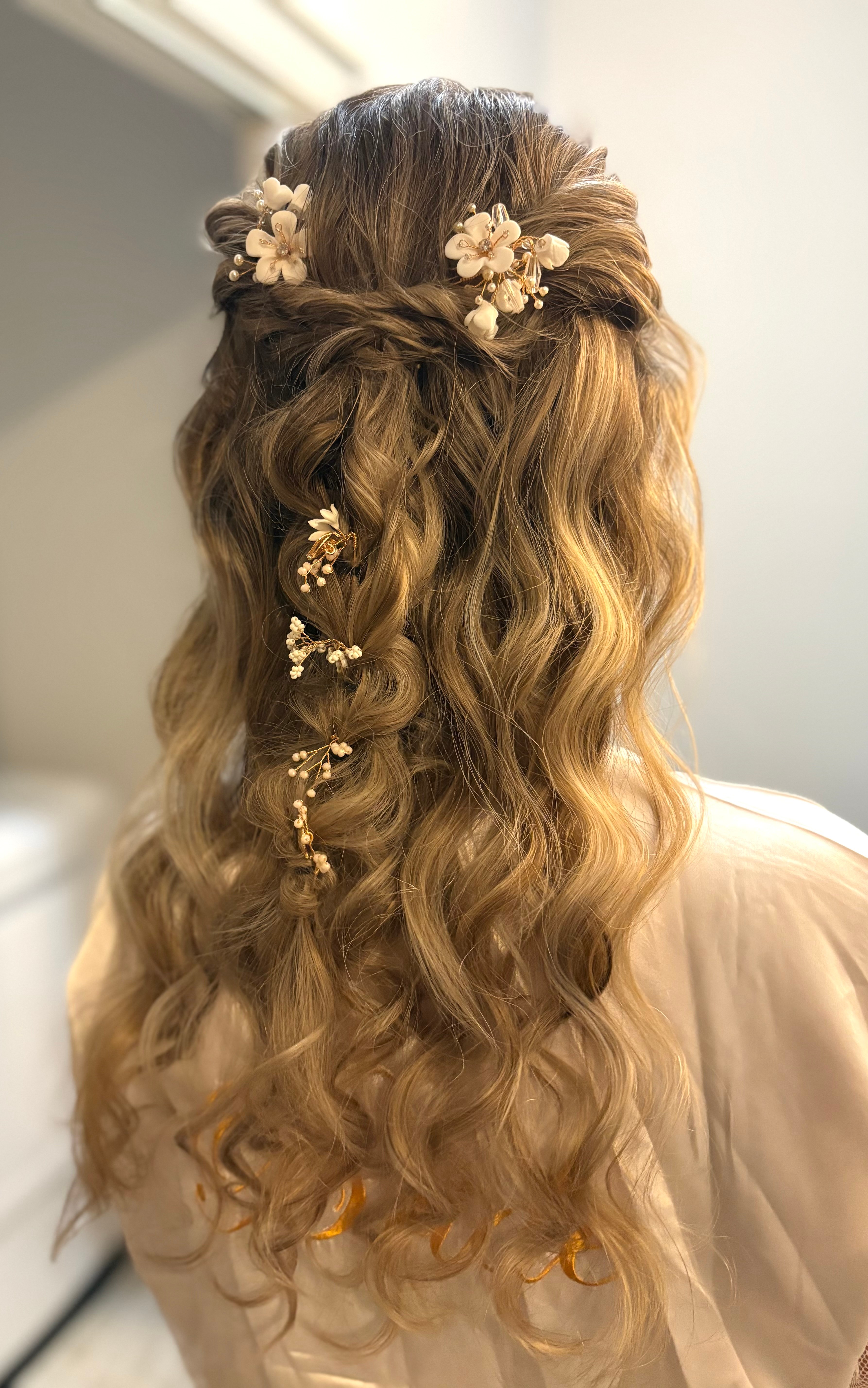 Back view of a woman with long, wavy hair decorated with floral accessories and small pearl embellishments.
