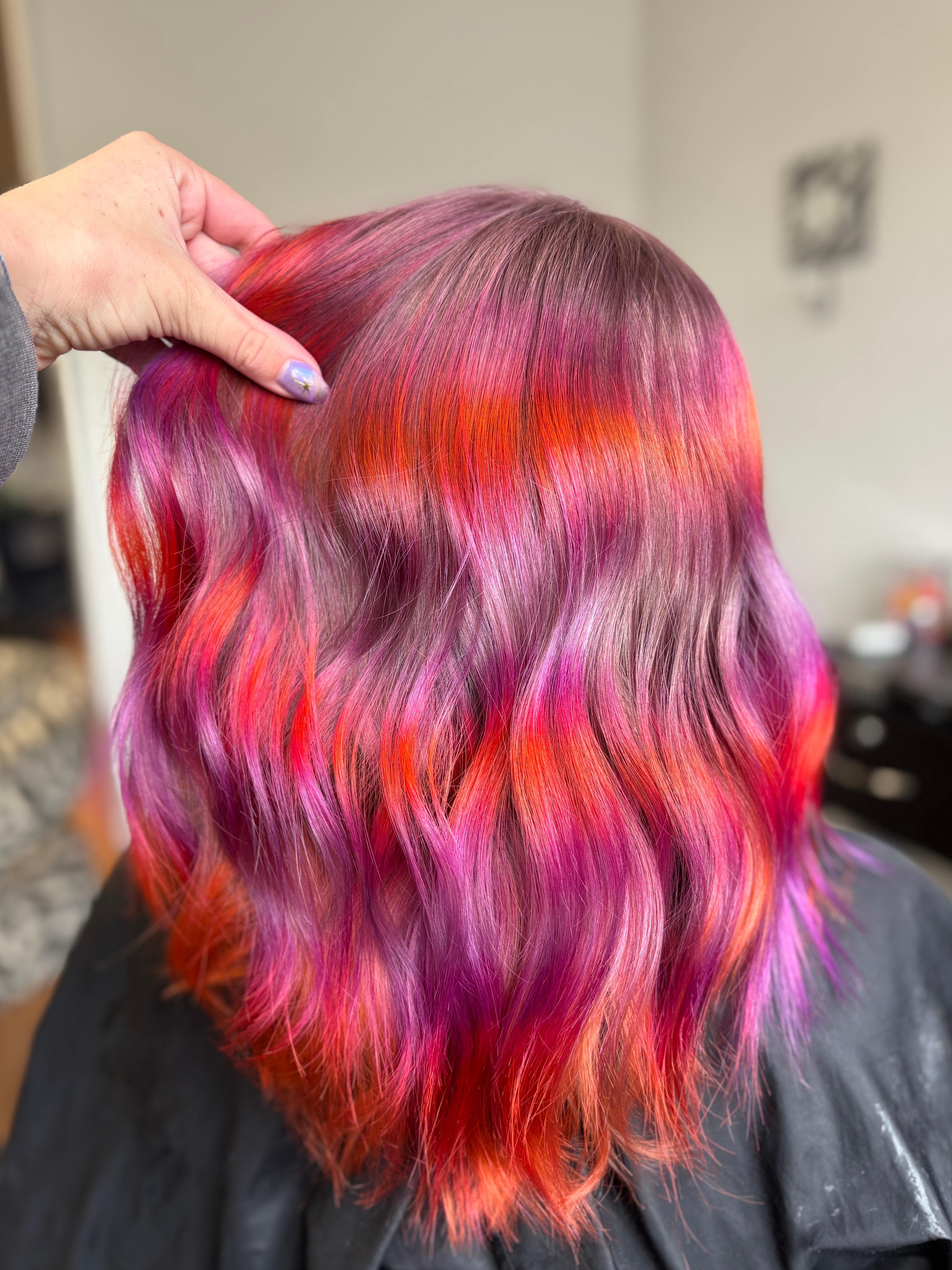 Back of a person's head with wavy, multicolored hair in pink, red, and purple shades.