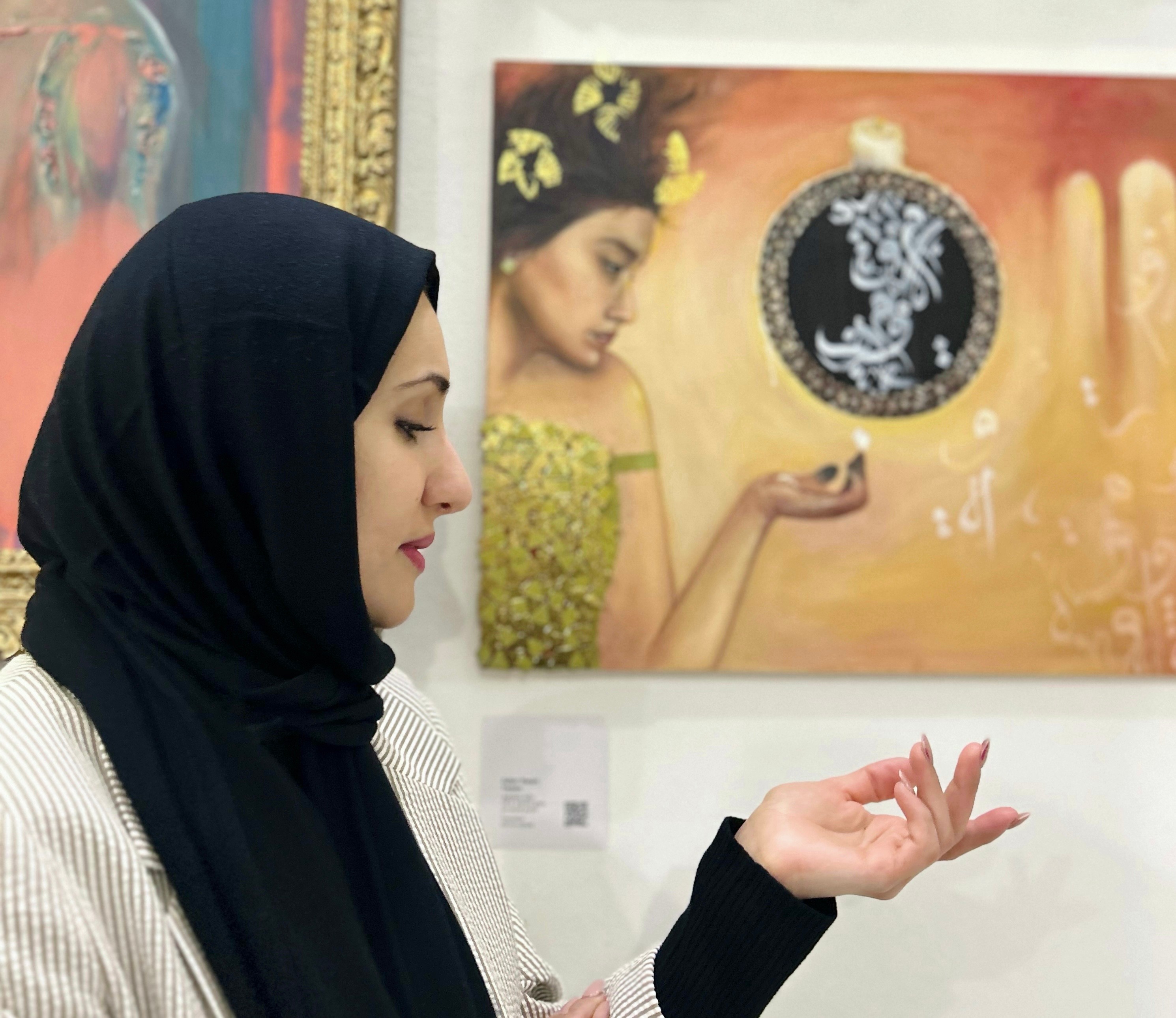 Woman wearing a black hijab and striped shirt looking at artwork in gallery, with her hand raised slightly.