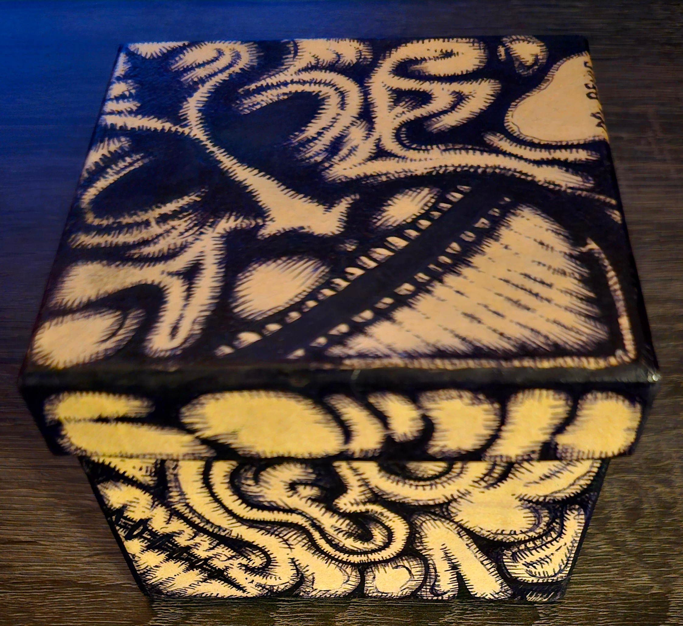Decorative box with black and white abstract swirling patterns on top and sides, placed on a dark wooden surface.