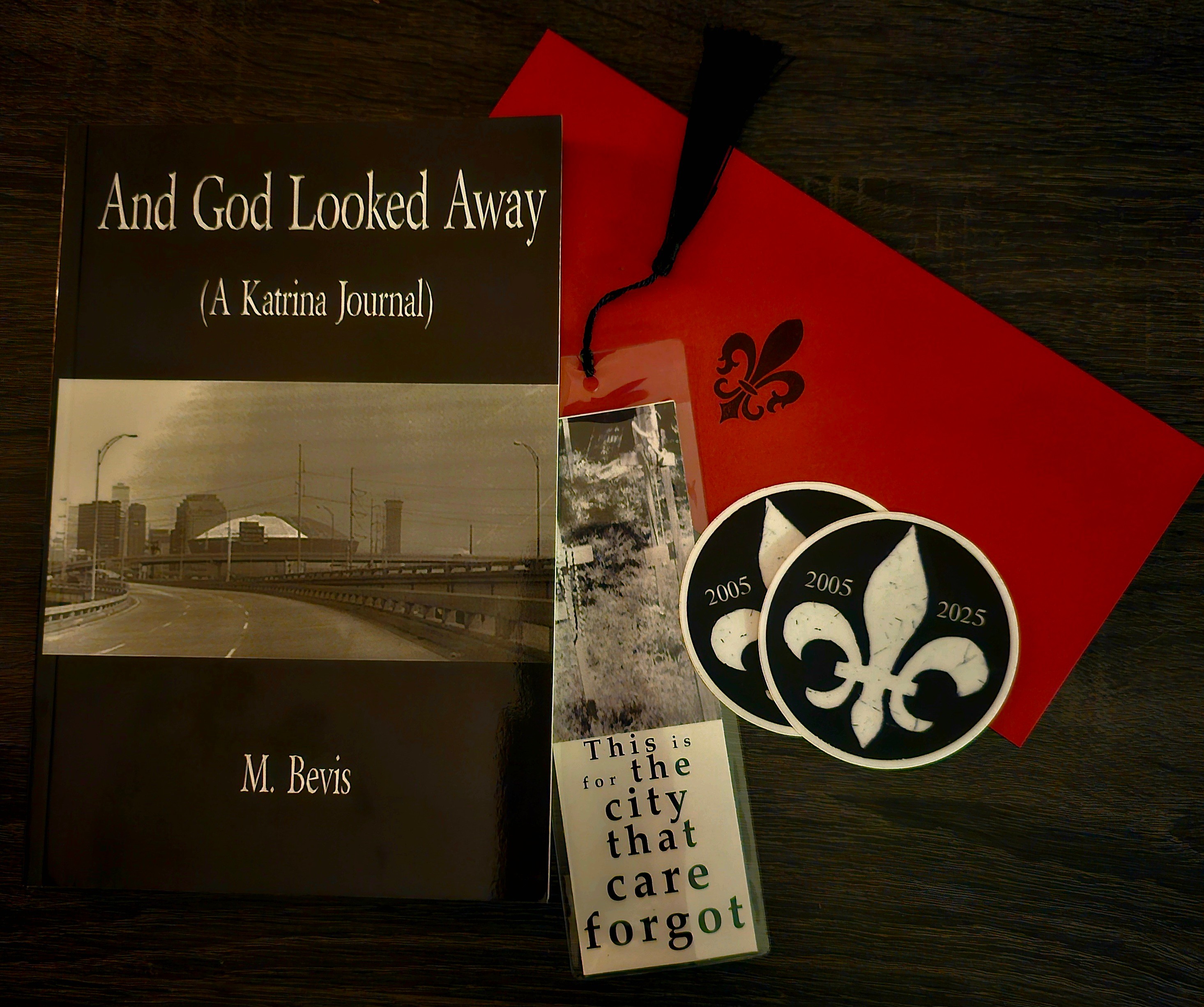 Book titled 'And God Looked Away' by M. Bevis, a red and black fleur-de-lis flag, a circular emblem with fleur-de-lis and years, and a small card with text. Word count: 20