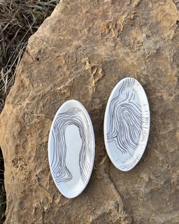 Two oval-shaped ceramic plates with blue swirl patterns on a large rock surface.