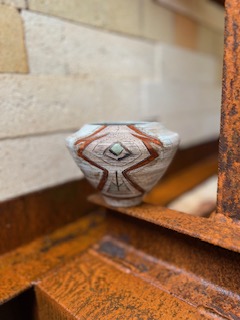 Small decorative bowl with geometric patterns on a rusty metal surface, against a brick wall background.