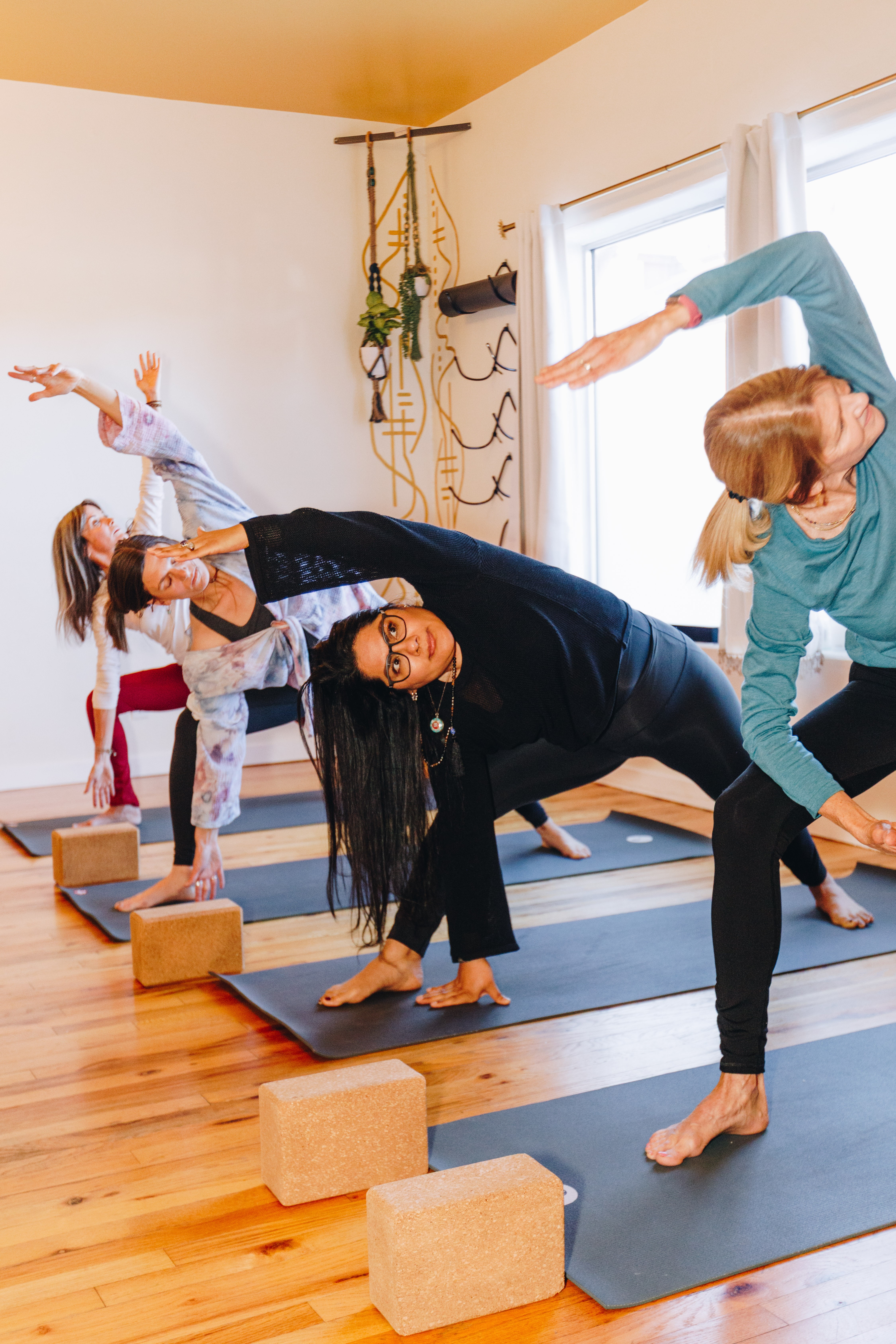 Group of people practicing yoga in a bright room with windows, mats, and yoga props, performing side stretches and poses.