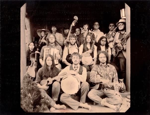 Group of people with musical instruments, some sitting and some standing, in a black and white photo.
