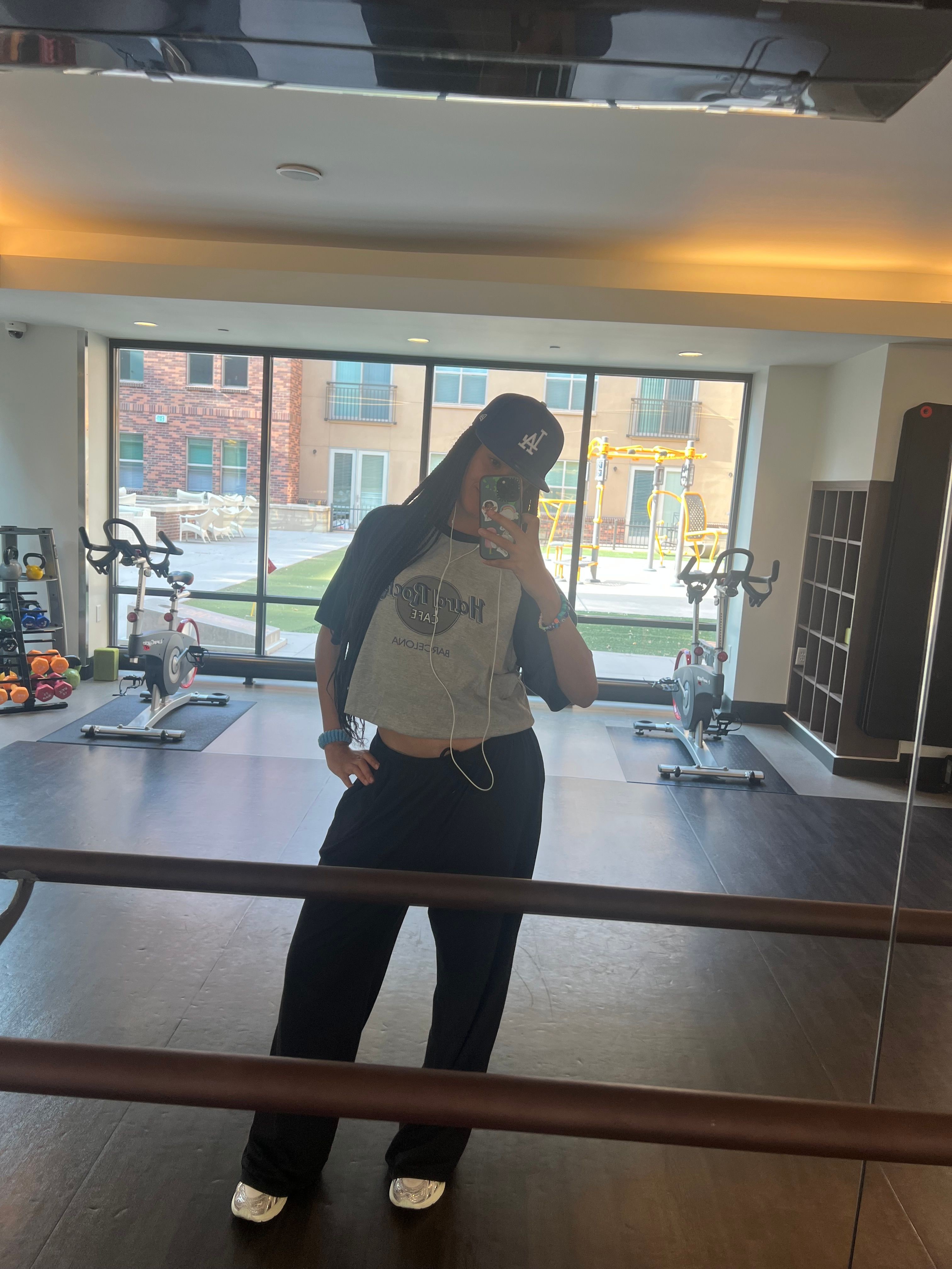 Person standing in a gym with large windows, exercise equipment, and a view of buildings outside.