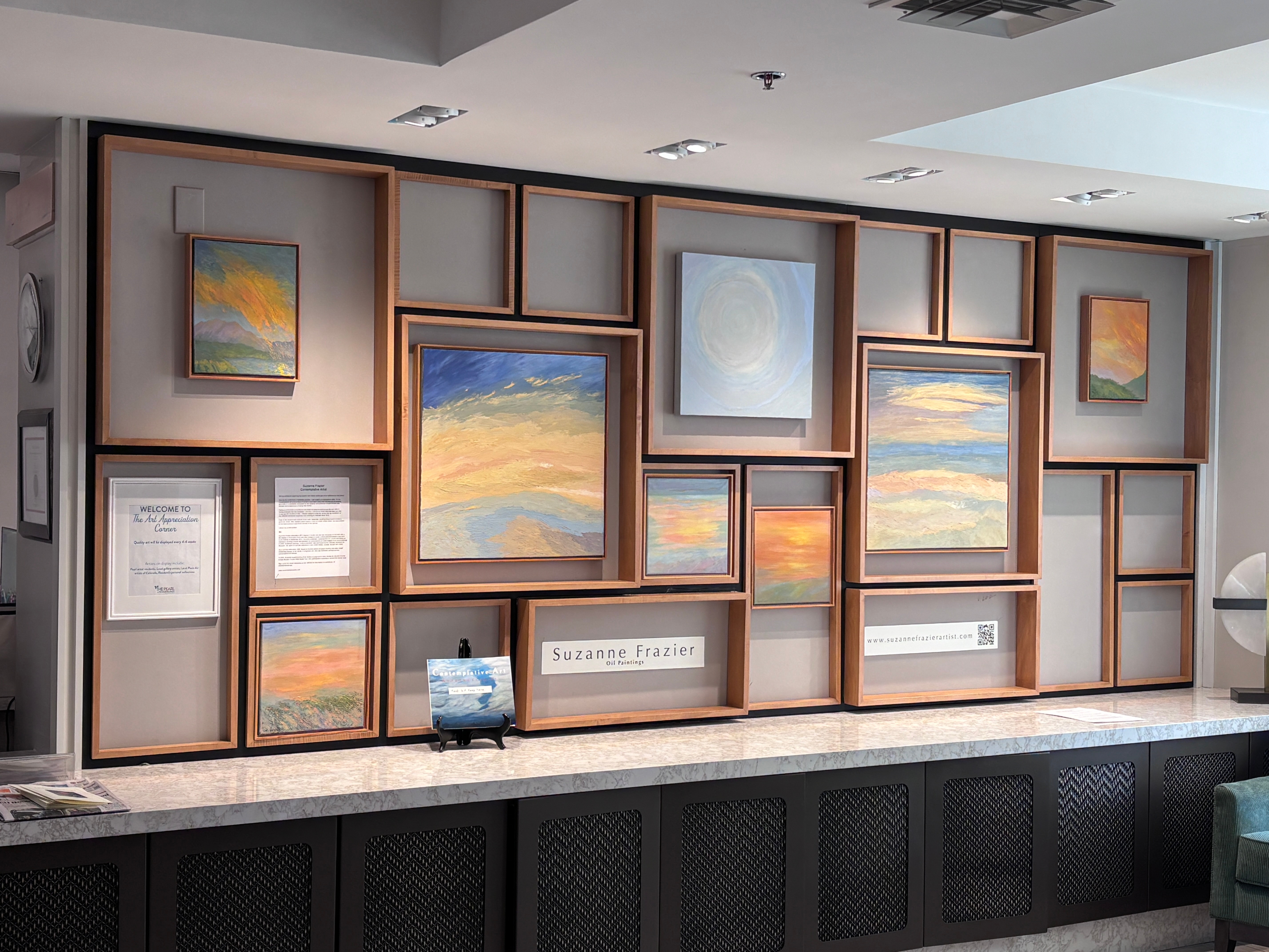 Wall with framed landscape paintings and certificates, with a small decorative object on a shelf below.