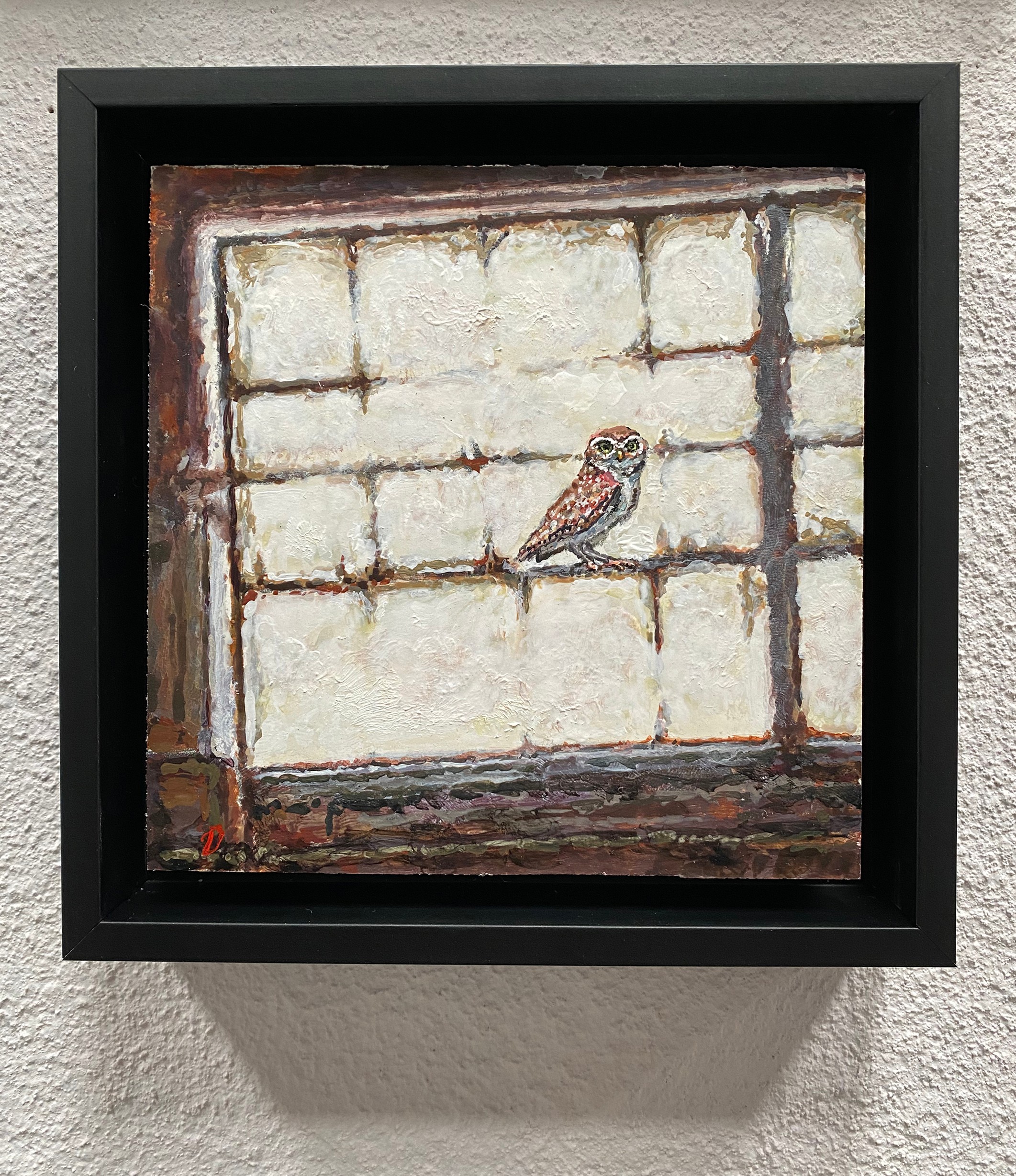 Painting of an owl on a brick wall, framed in black, with textured white bricks and dark mortar, hung on a wall.