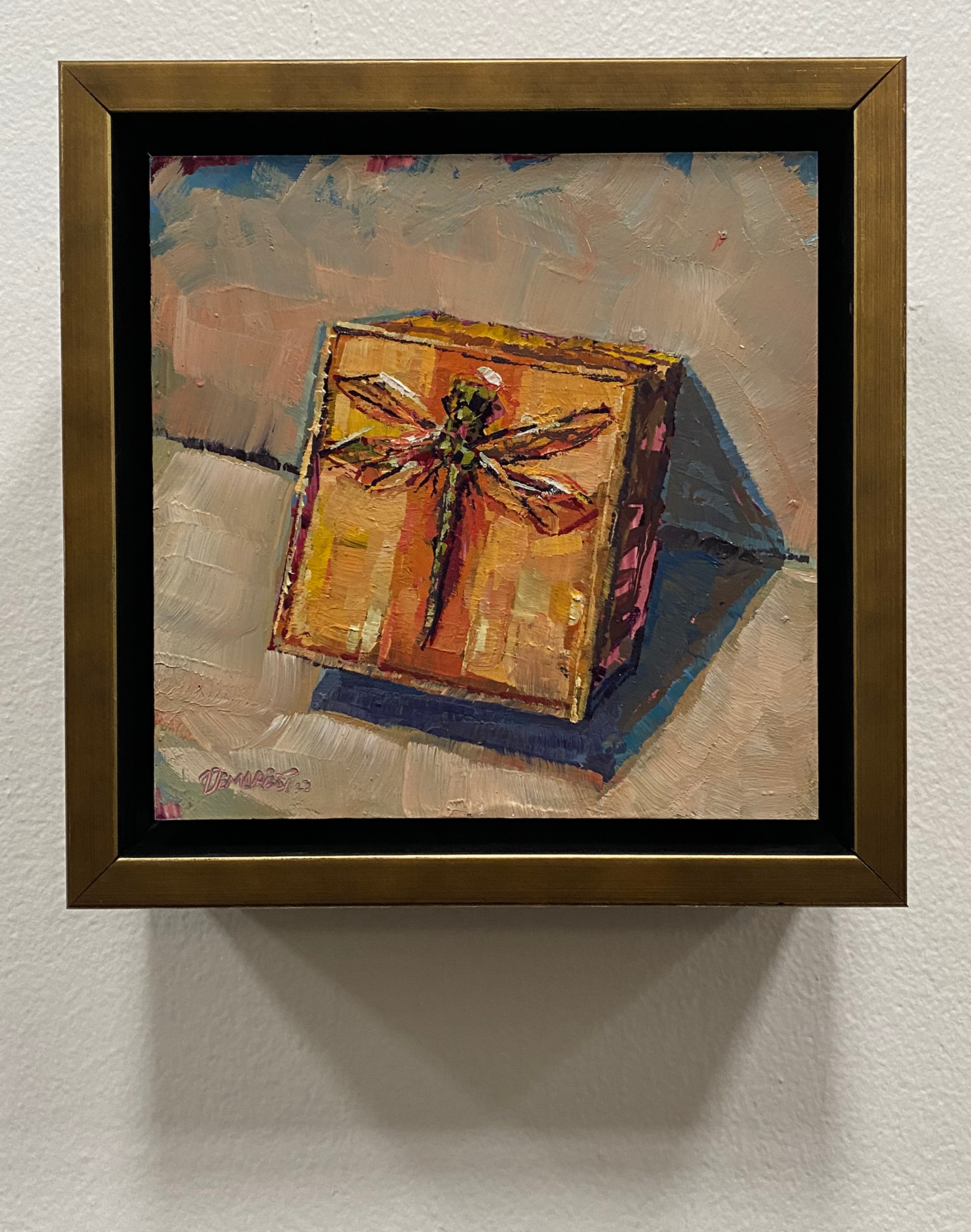 Painting of a gift box with a ribbon, placed on a surface with a shadow, in a frame on a wall.