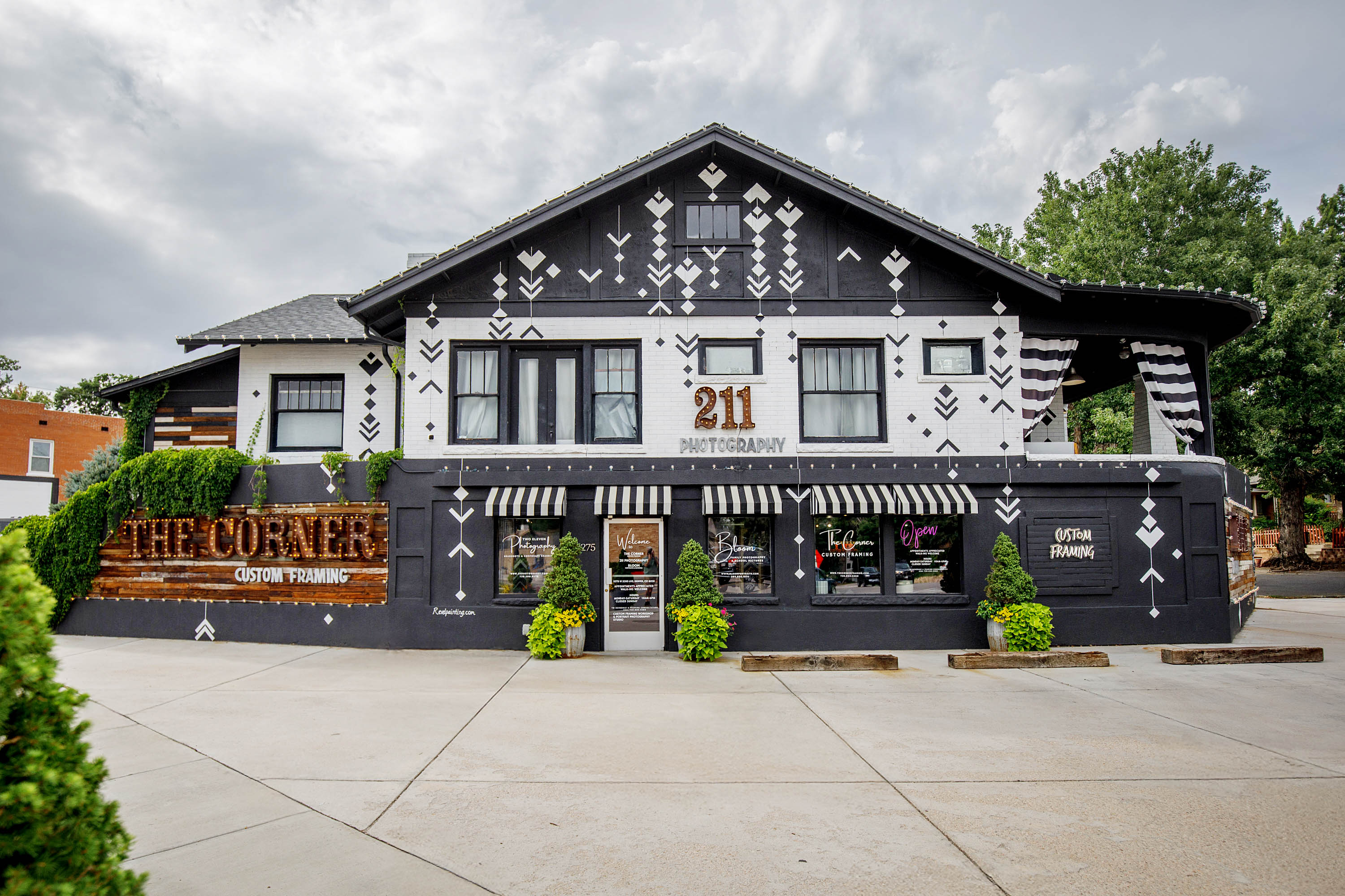 Two-story building with black and white geometric patterns, a sign reading 'THE CORNER,' and potted plants outside.