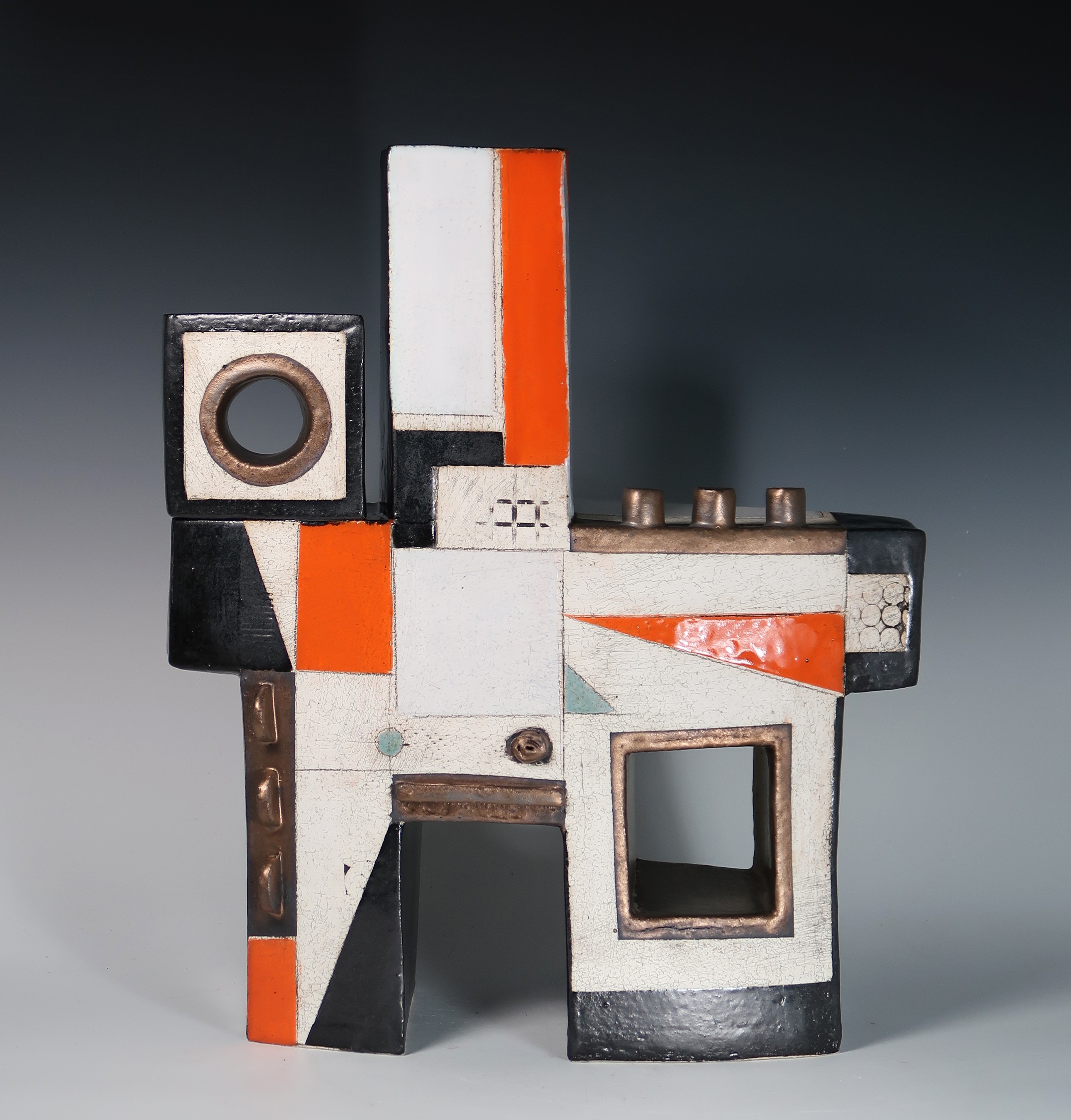 Abstract geometric sculpture with black, white, orange, and gray shapes, including a square hole and circular element, on a dark background.