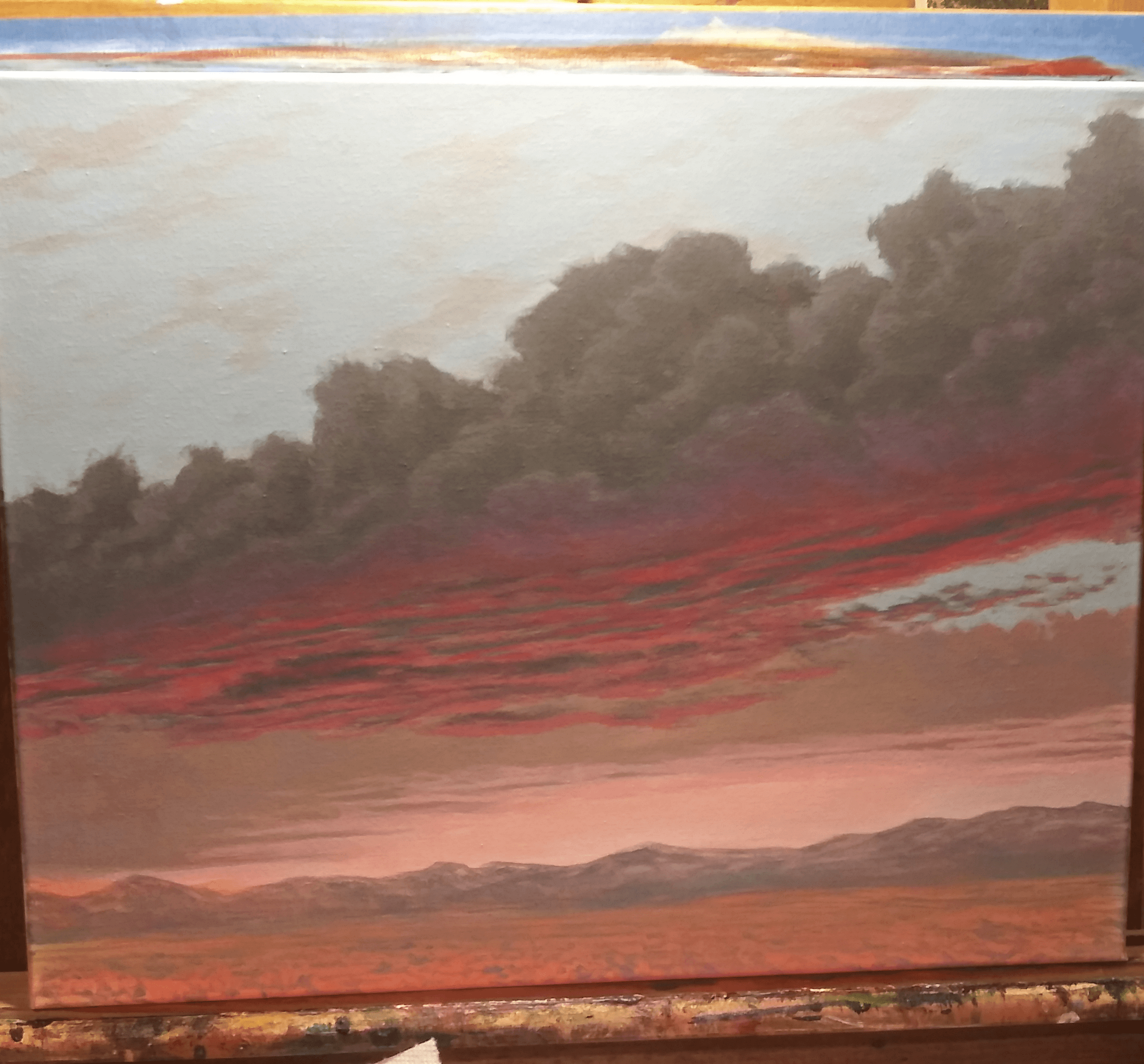 Cloudy sky with dark clouds over a landscape with mountains and a colorful sunset or sunrise, with pink and red hues.