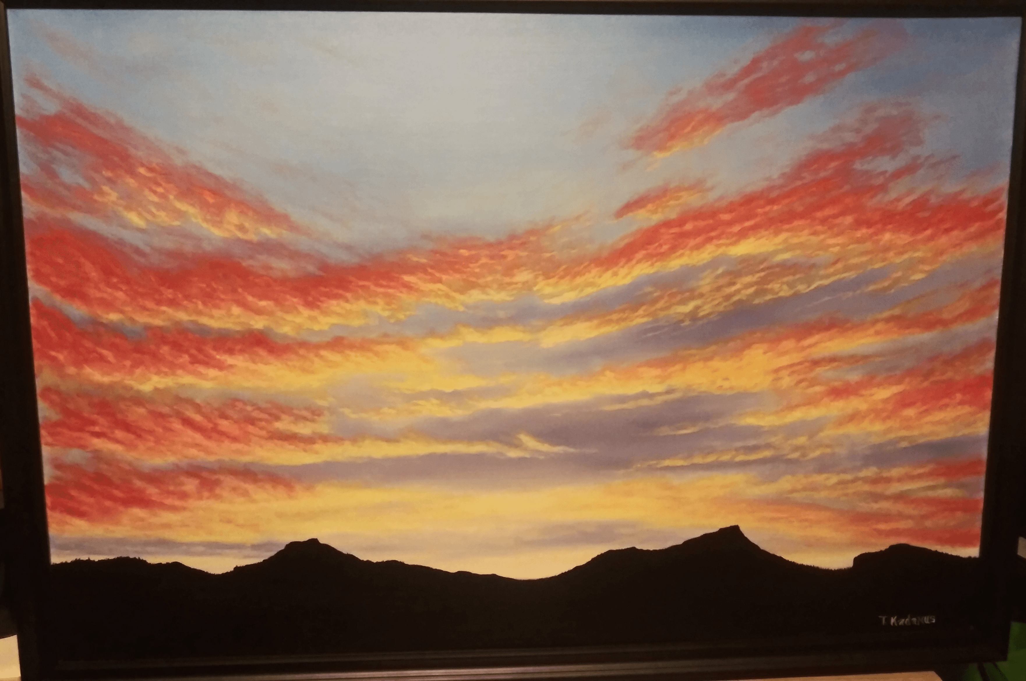 Landscape painting of a sunset sky with colorful clouds above dark mountain silhouettes.