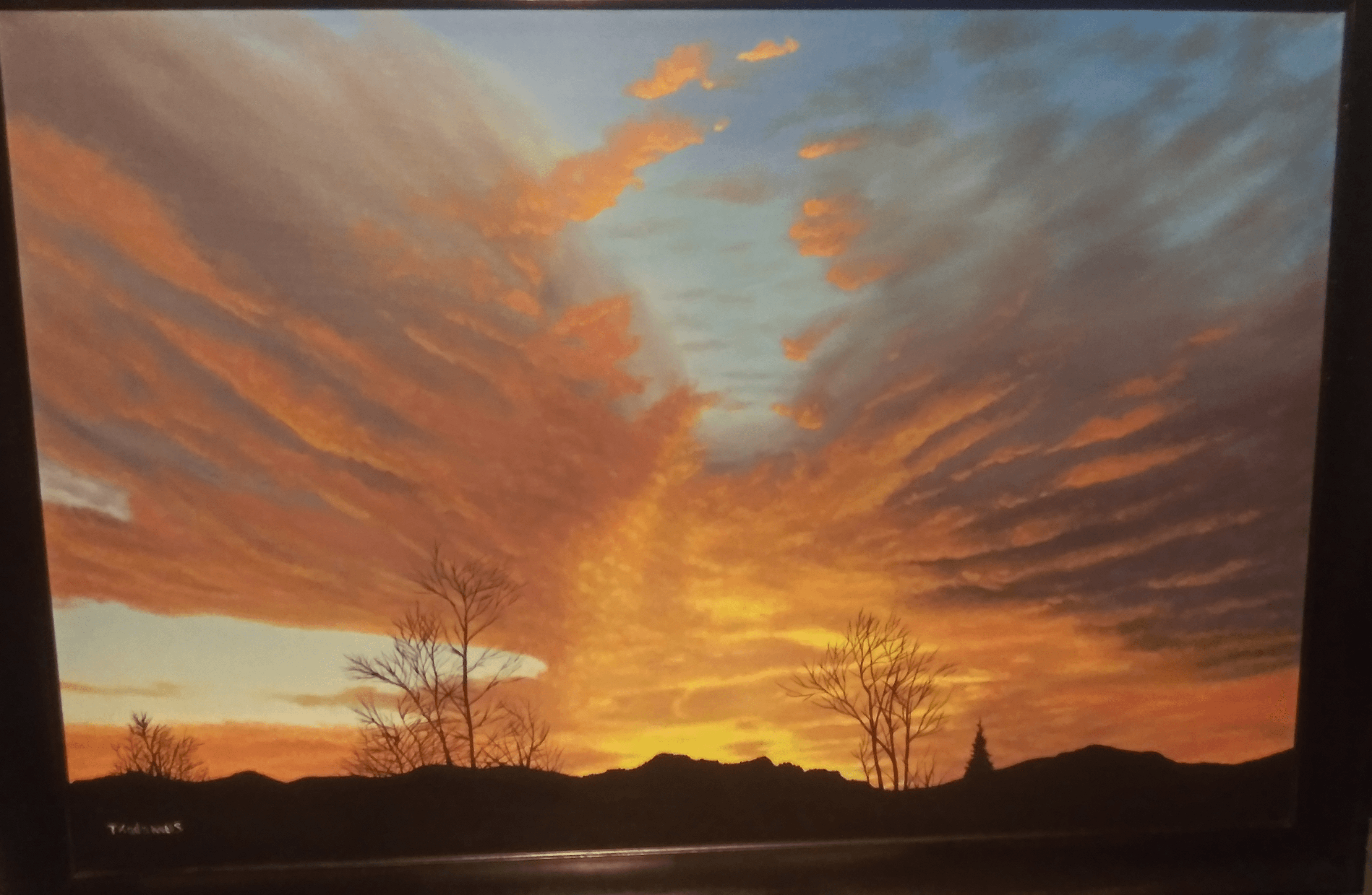 Sunset sky with orange, pink, and blue clouds over a landscape with trees and hills.