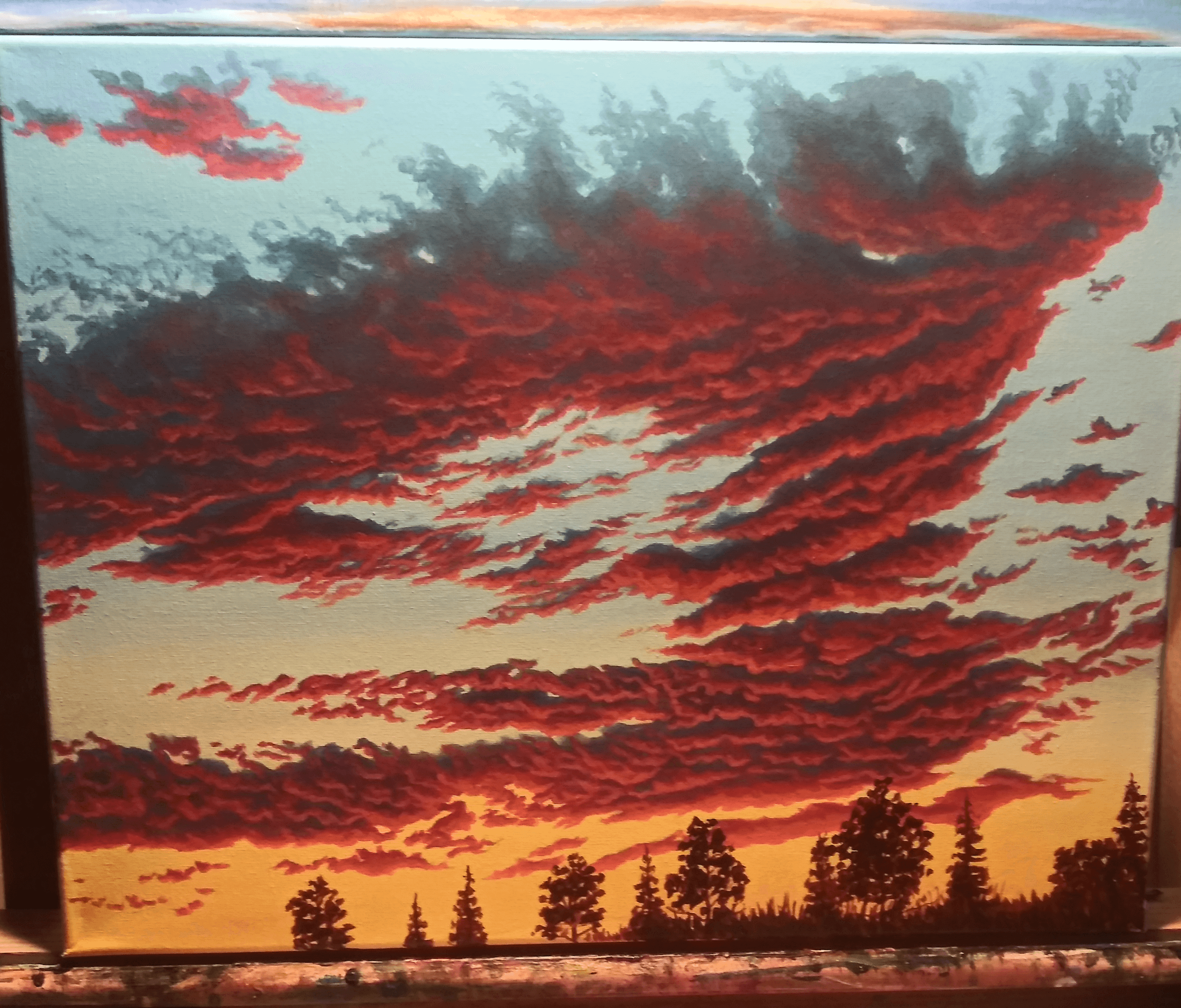 Colorful sunset sky with red and orange clouds above silhouetted trees, vibrant and dramatic scene.