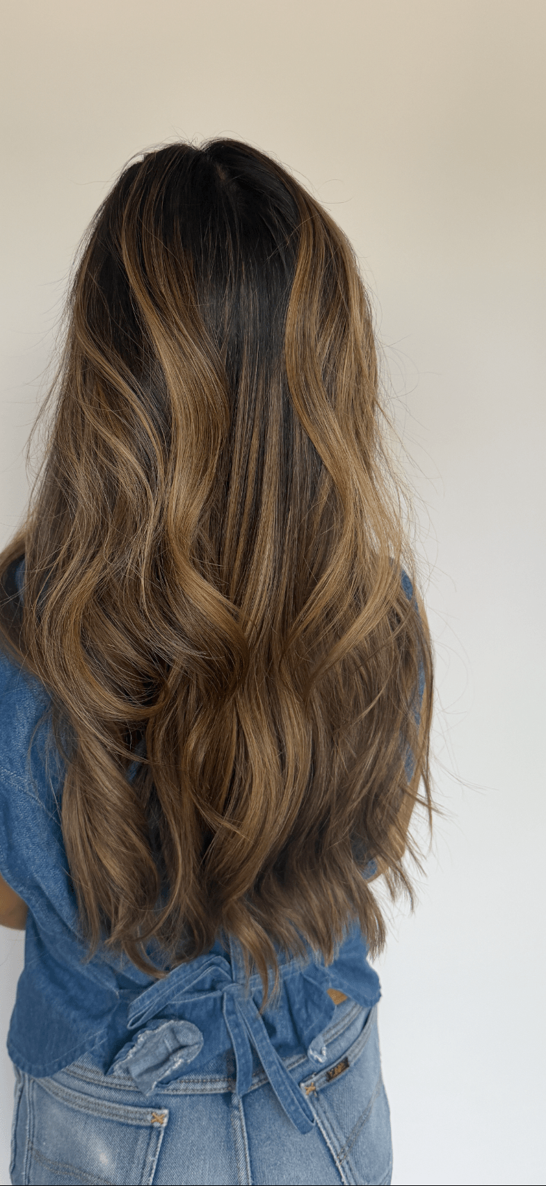 Back view of a person with long, wavy brown hair wearing a blue top and jeans.