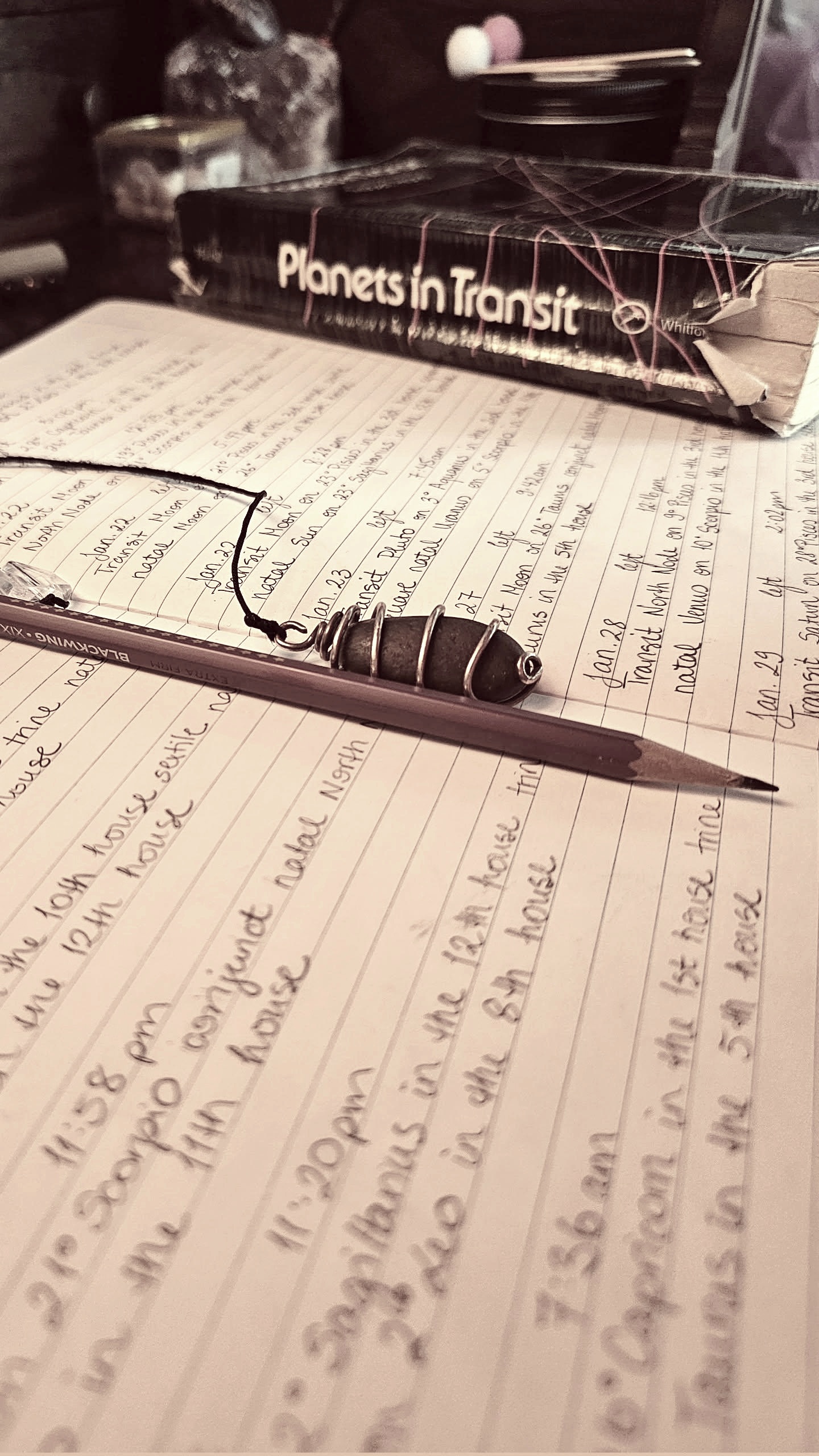 Open notebook with handwritten notes, pen resting on pages, and a book titled 'Planets in Transit' in the background.