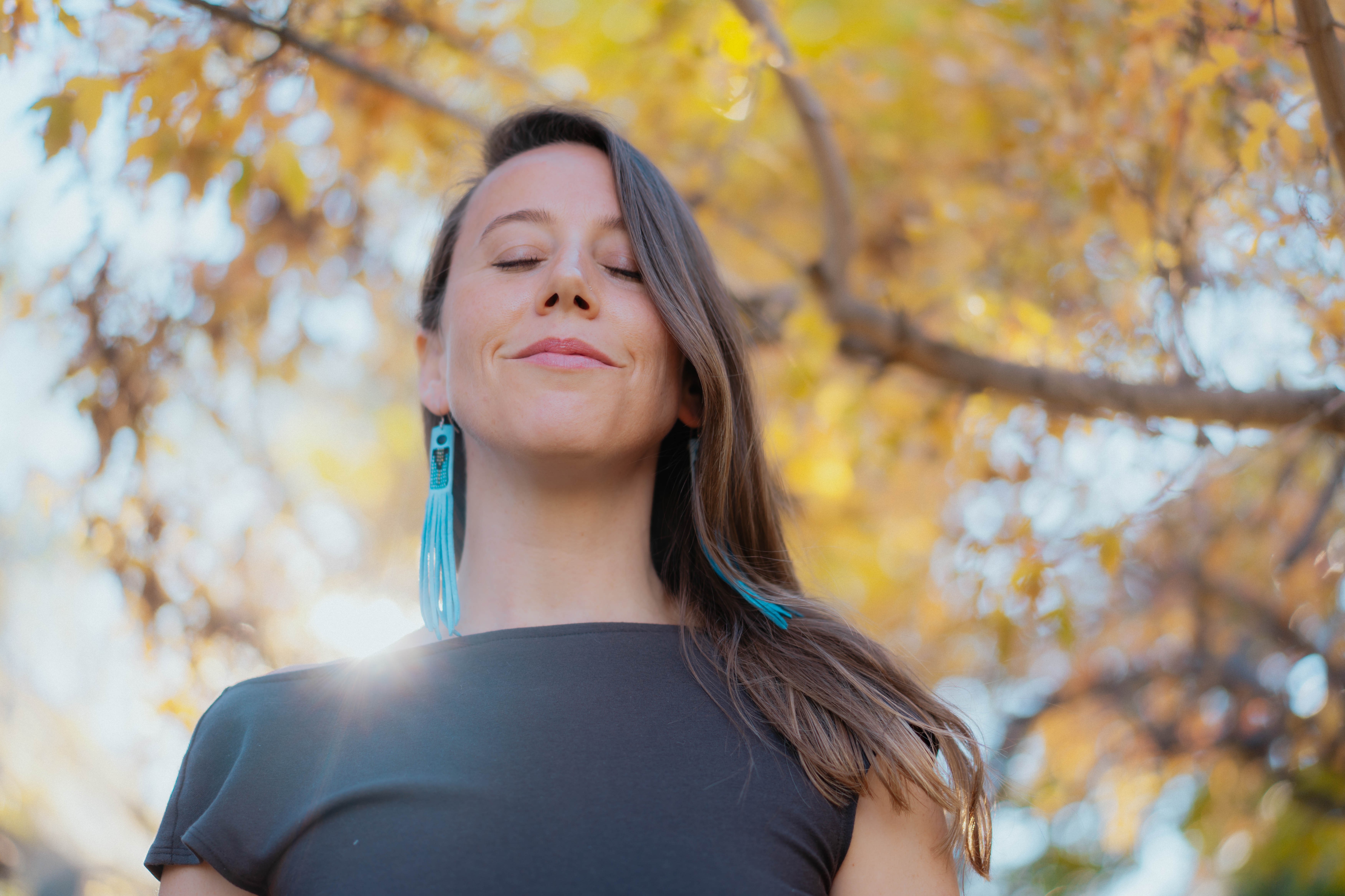 Woman with closed eyes smiling outdoors with autumn leaves in background