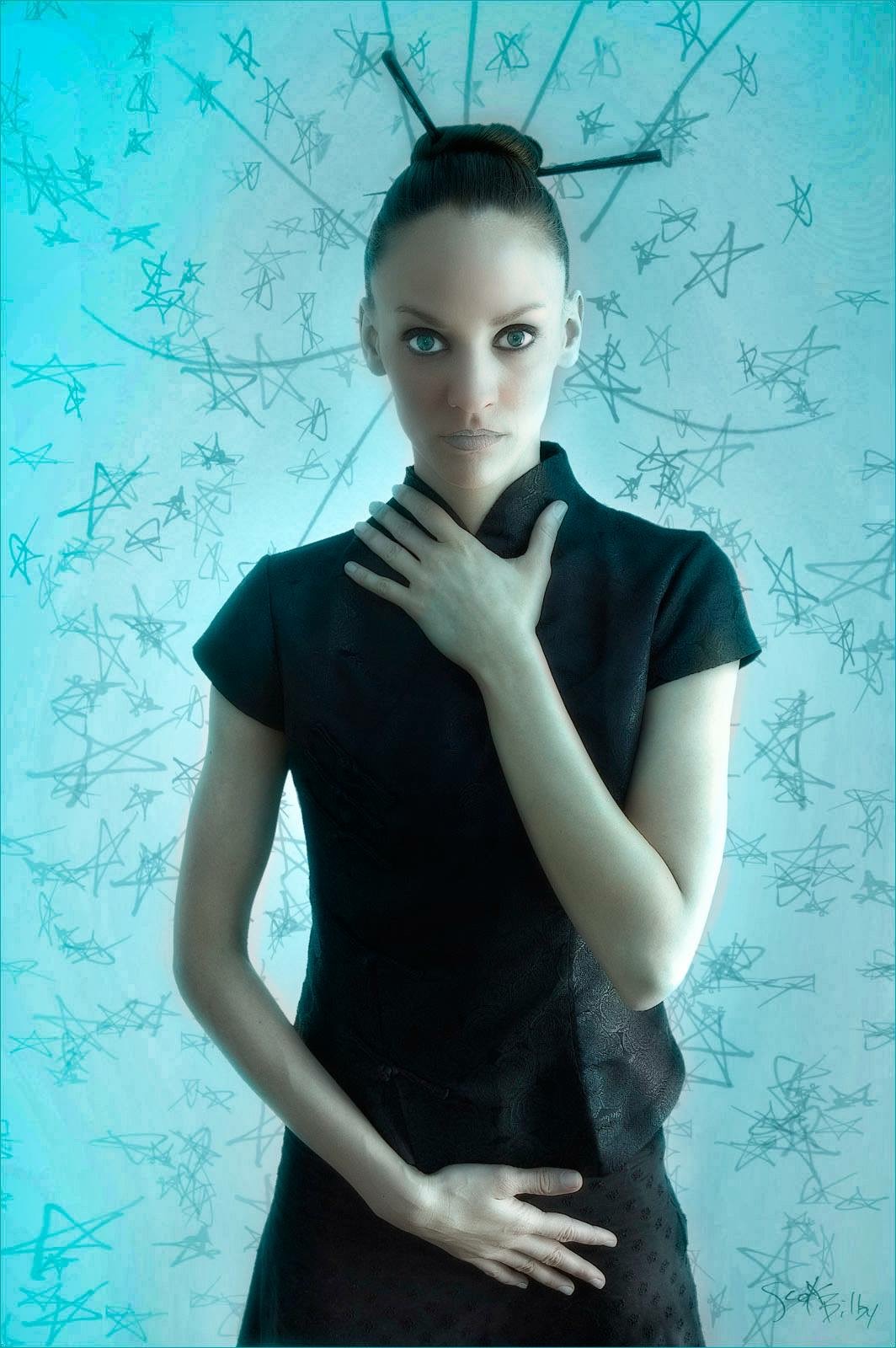 Young woman with dark hair in a bun, wearing a black dress, standing against a light background with star-like patterns.