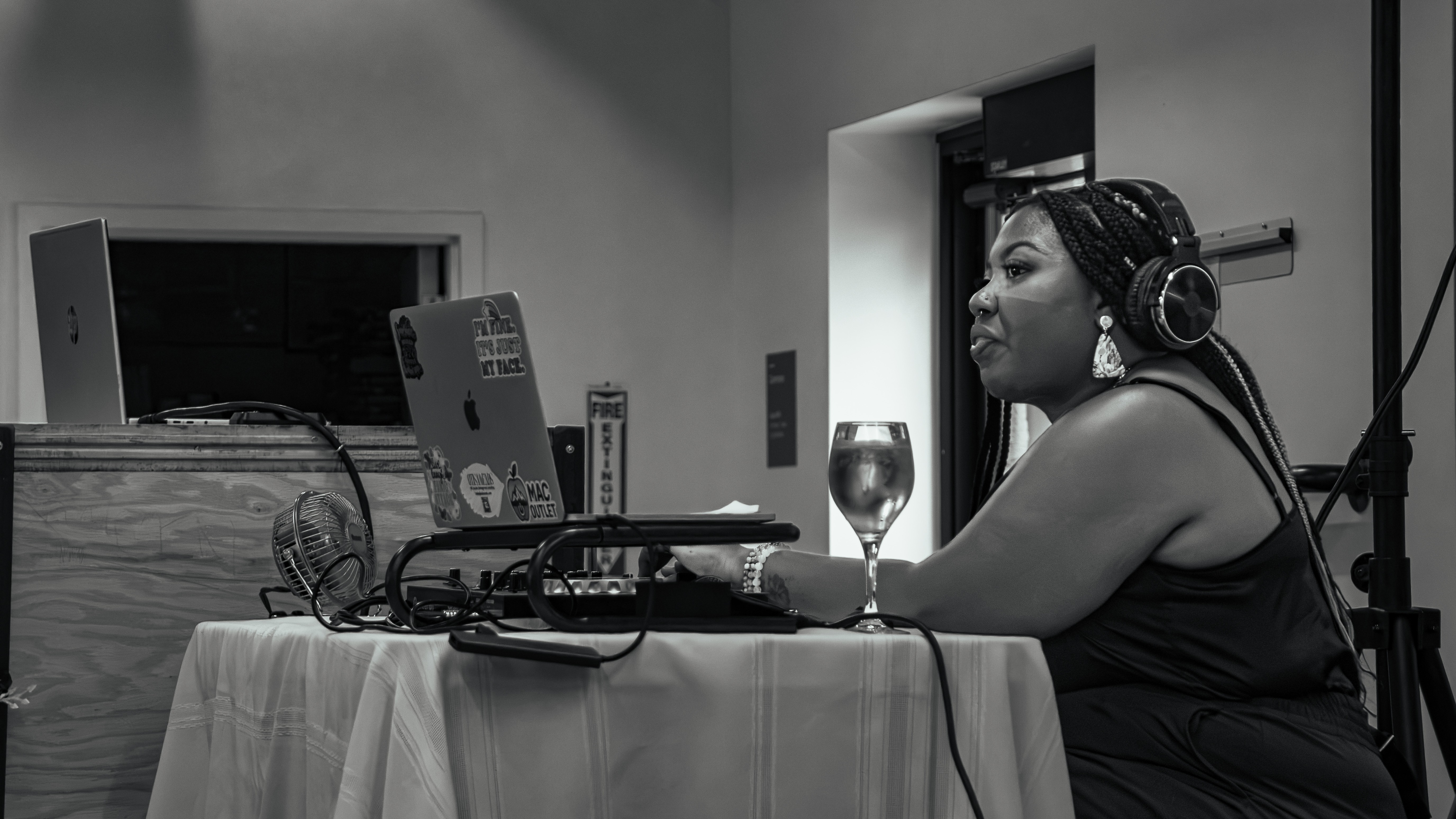 Woman with headphones sitting at a table with a glass of wine, equipment, and a laptop, in a recording studio.