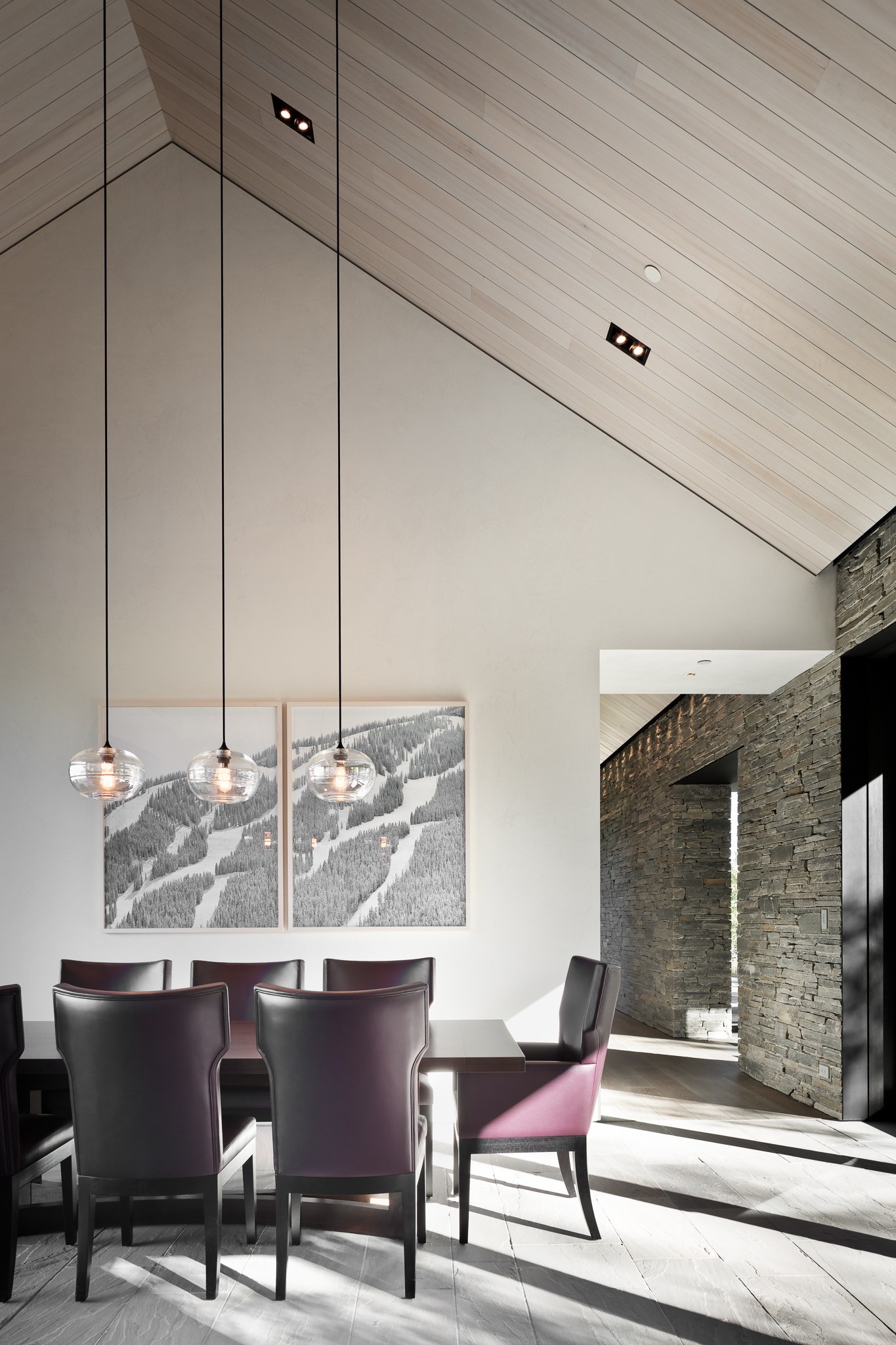 Dining area with a round table, six chairs, artwork on the wall, and large windows letting in natural light.