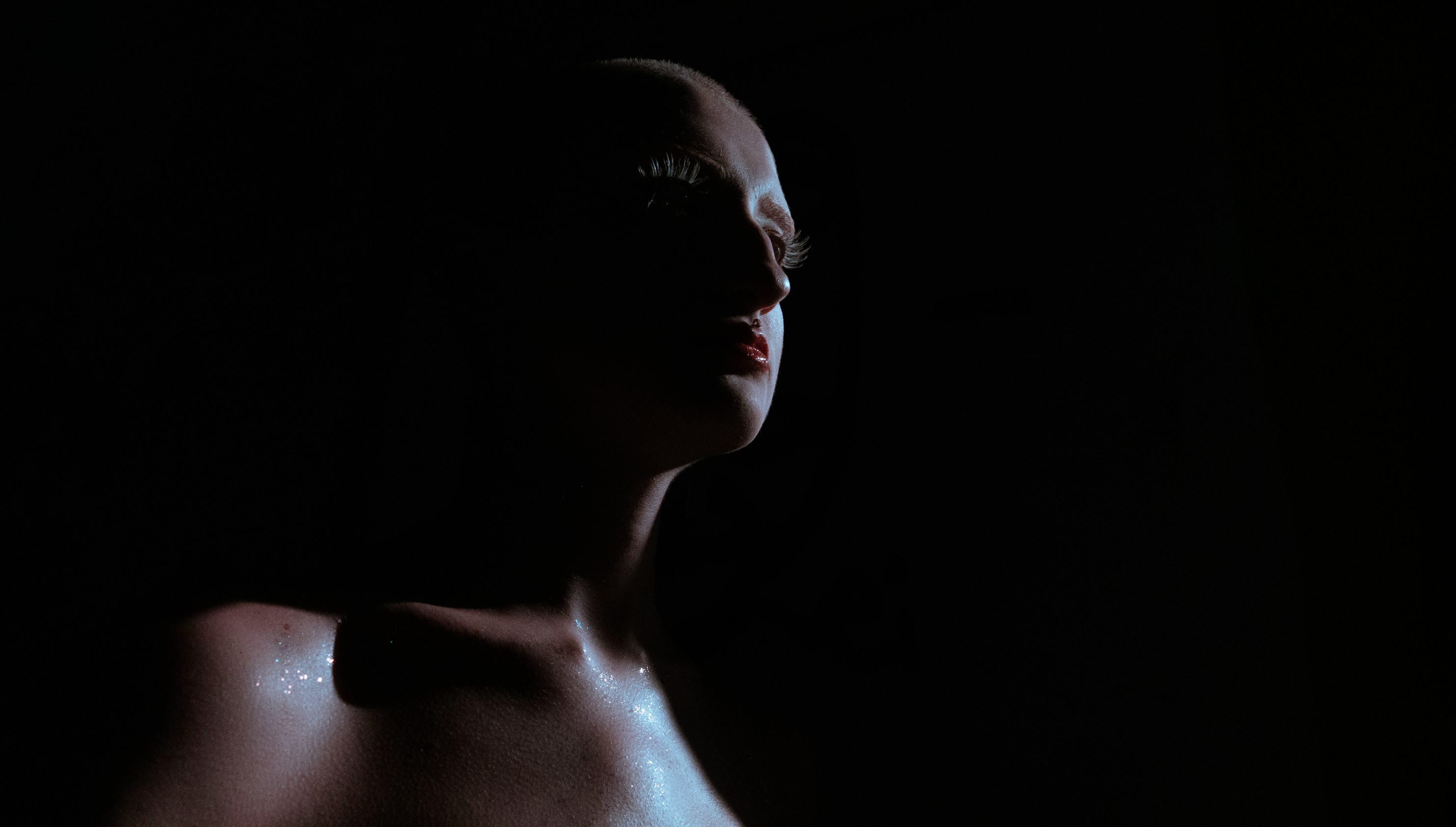 A woman with minimal lighting highlights her face and shoulder against a dark background.
