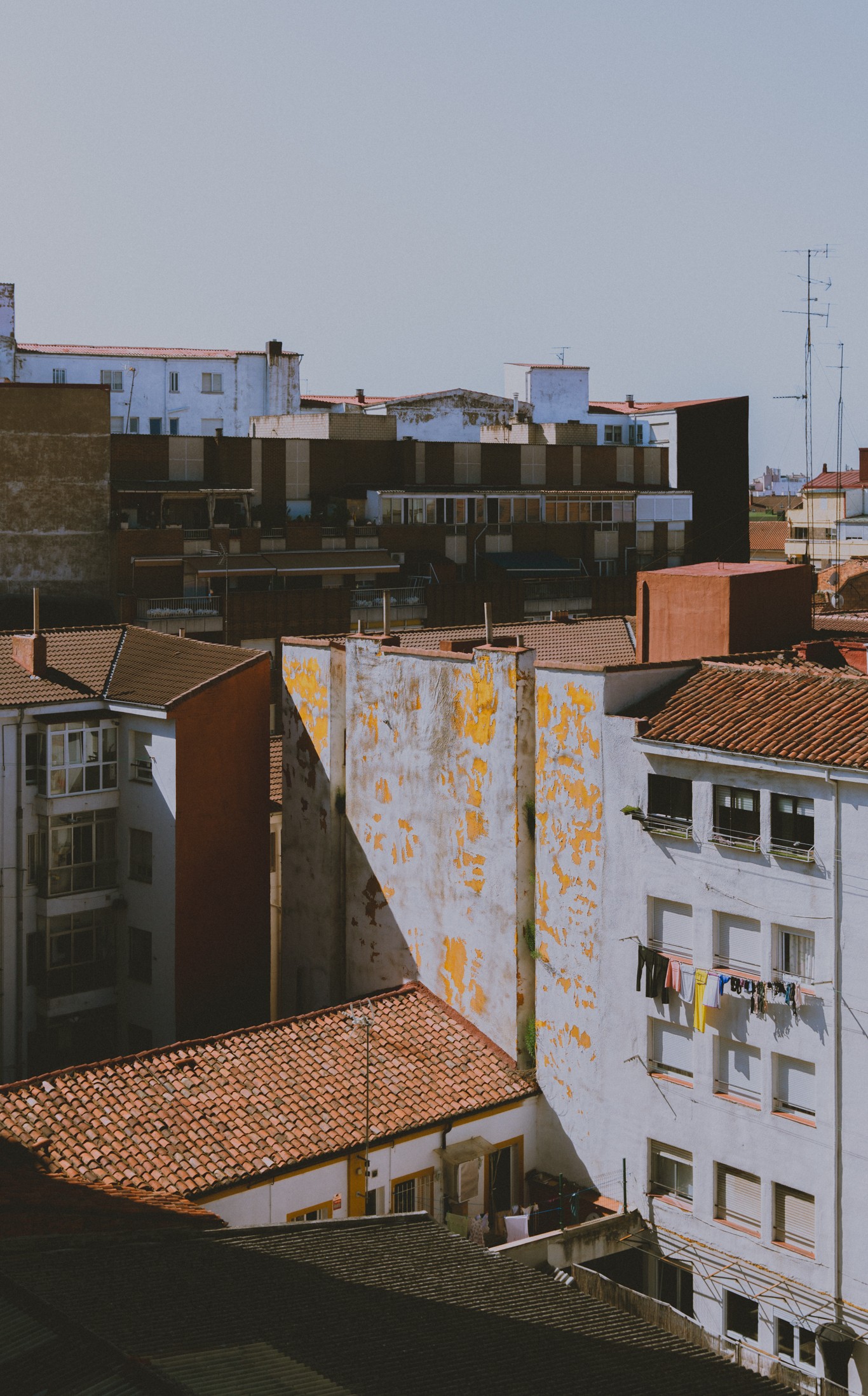 Cityscape with buildings, rooftops, and a clear sky, viewed from below, with some buildings showing signs of wear.