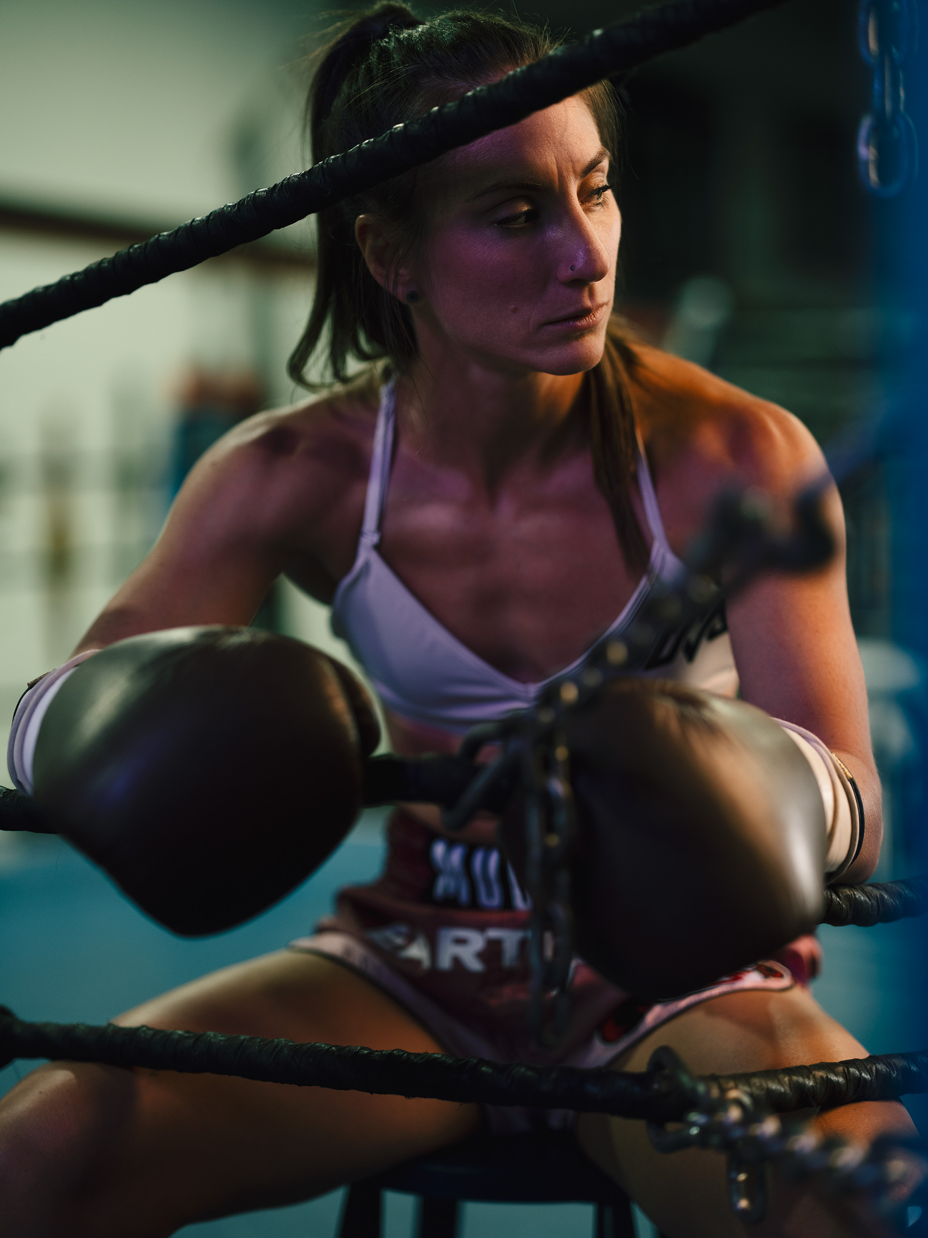 Female boxer in boxing gloves and sports bra, sitting in a boxing ring, focused and determined.