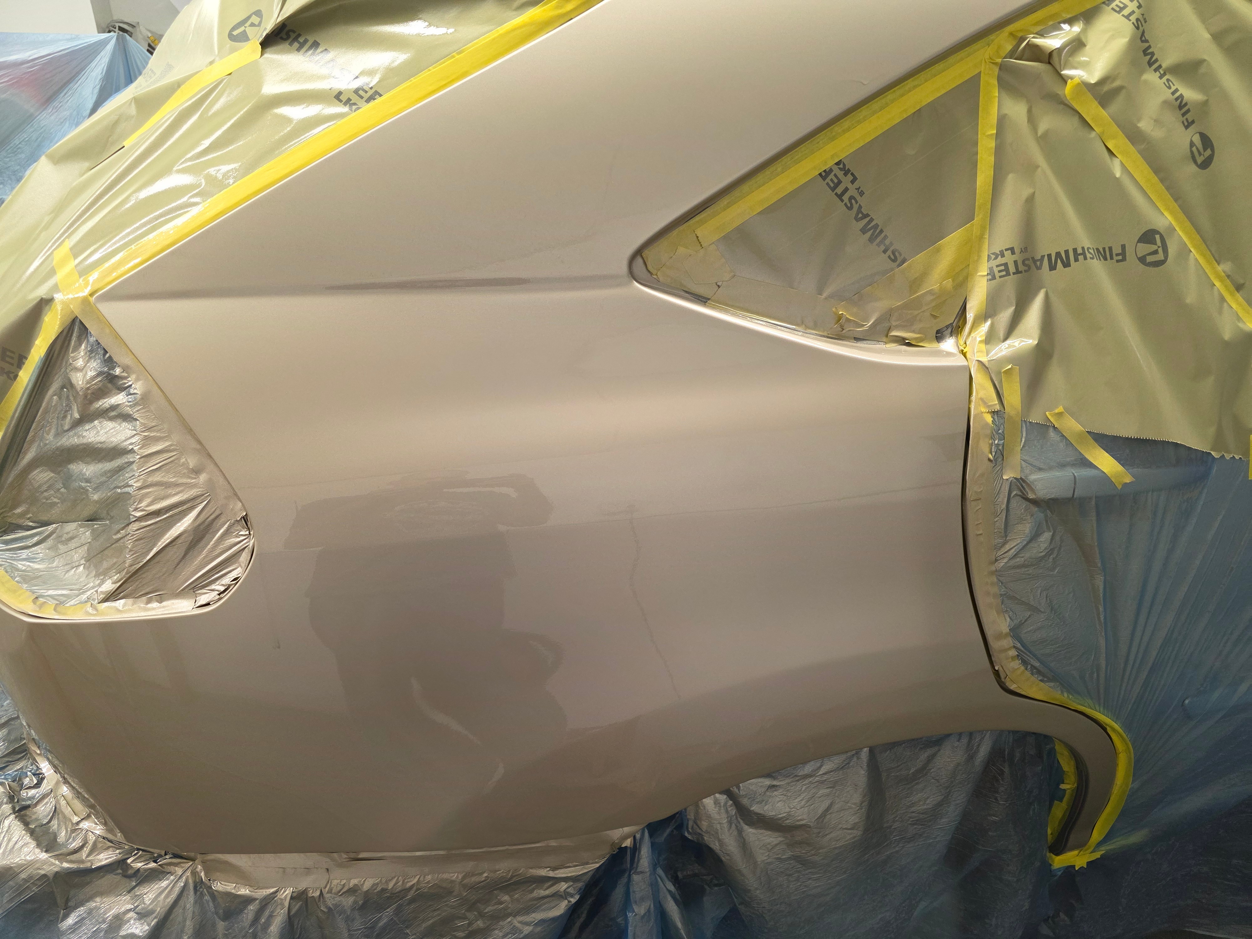 Car door painted with a smooth, reflective surface, surrounded by masking tape and protective coverings during painting process.