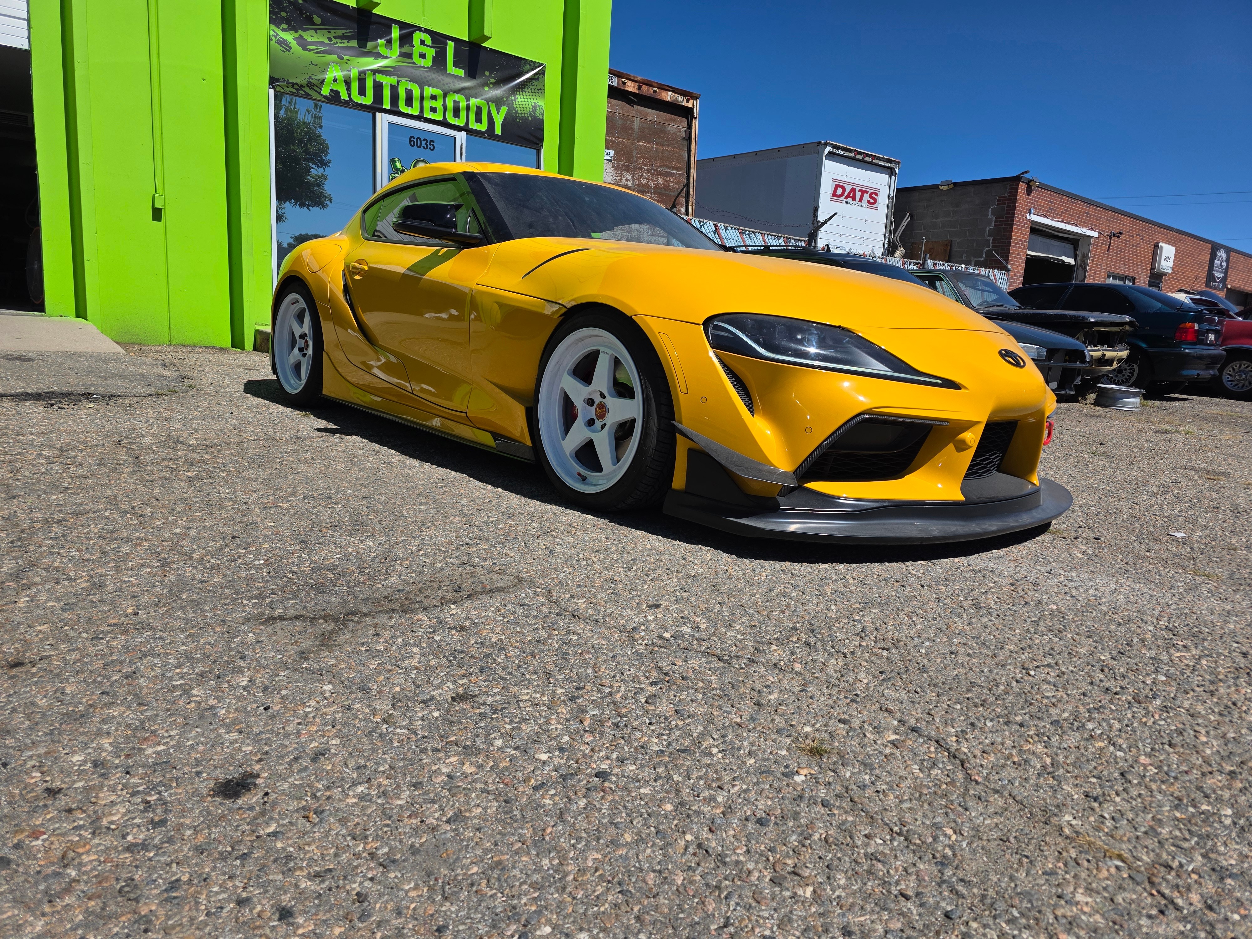 Yellow sports car parked outside a building with a green door, under a clear blue sky.