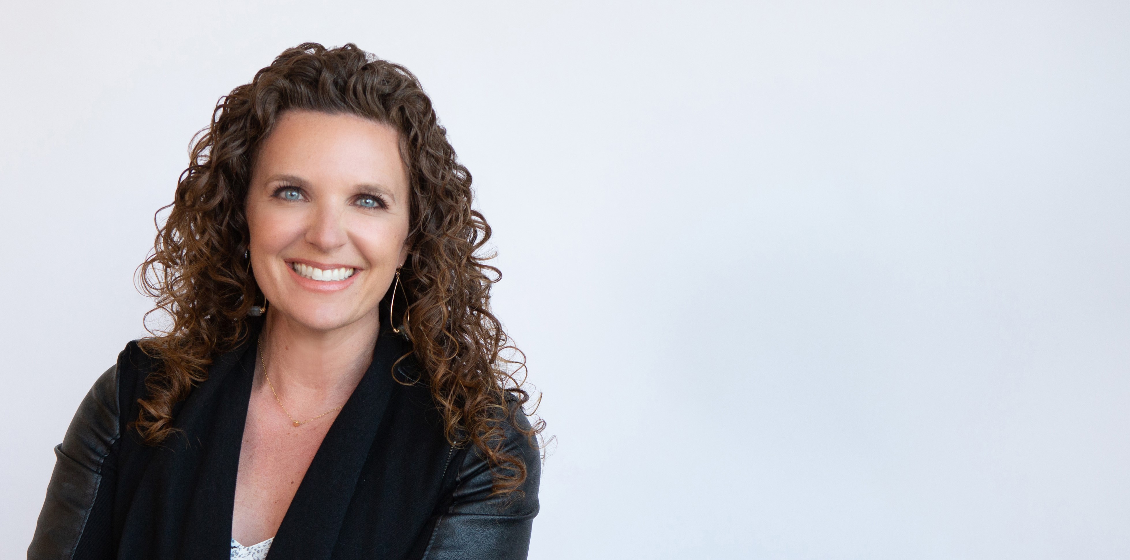 Smiling woman with curly hair wearing a black jacket against a plain white background.