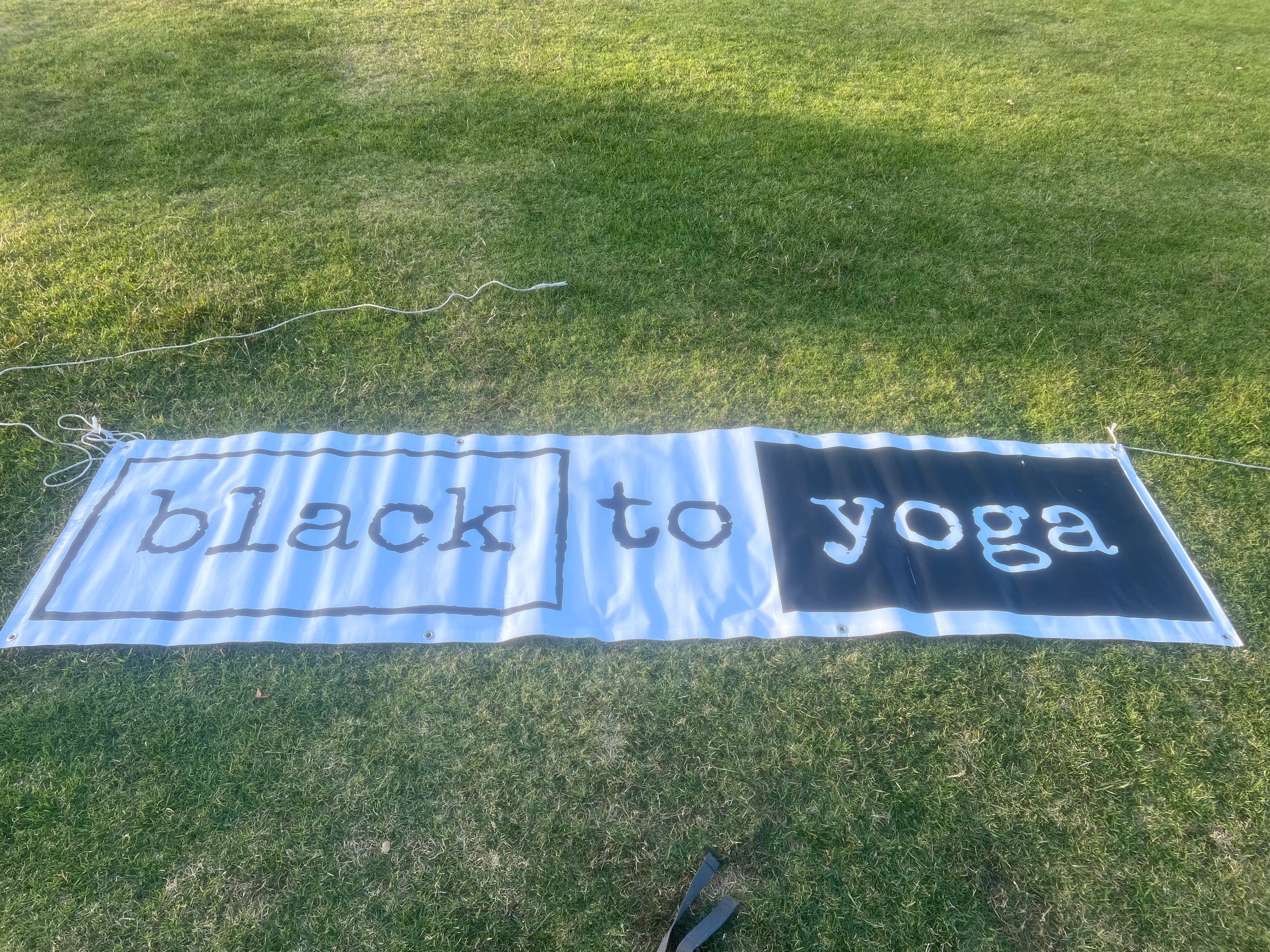 A towel on grass with the words 'black to yoga' printed on it, with the towel slightly wrinkled.