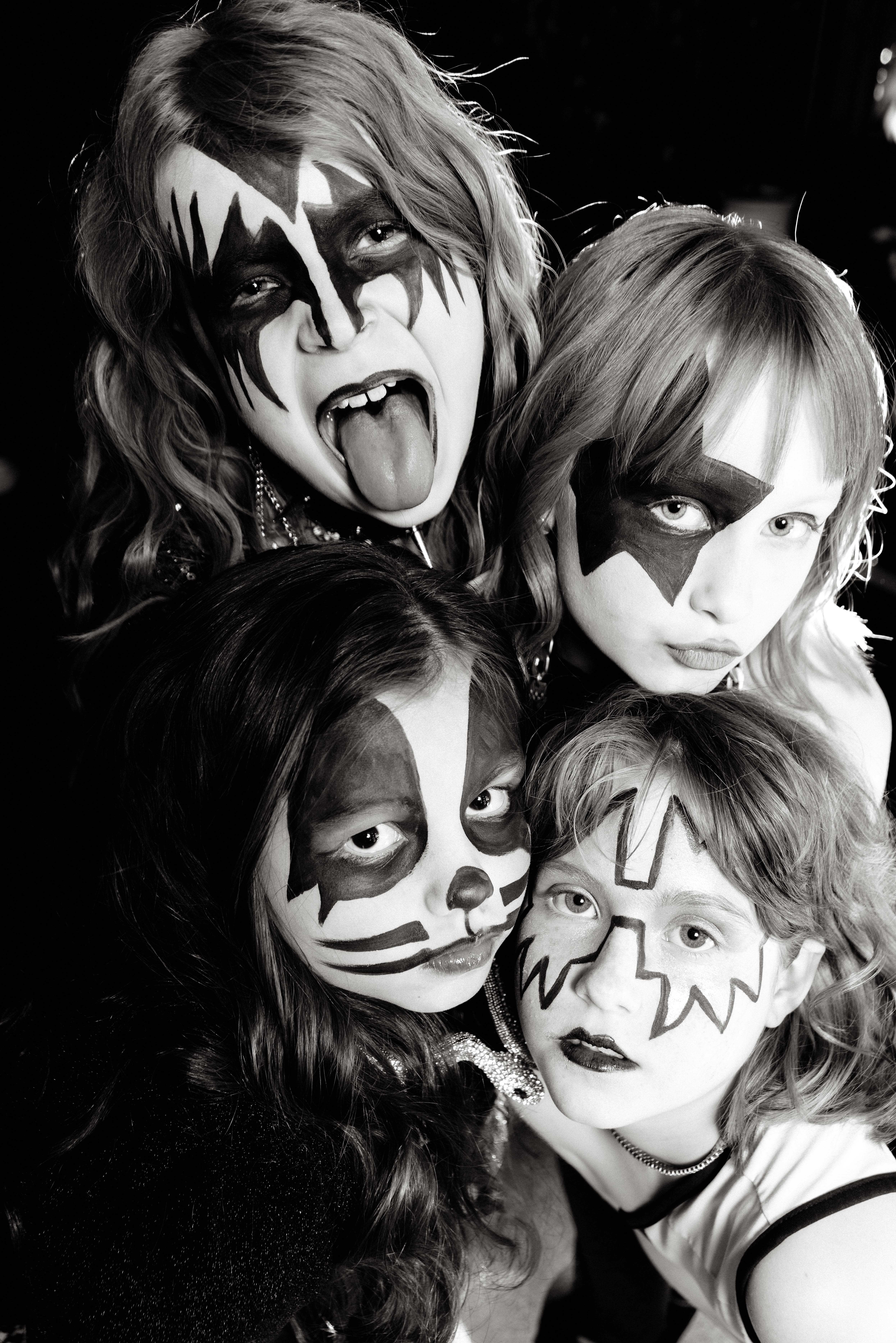 Four people with face paint, two with black and white designs, one with tongue out, in black and white.