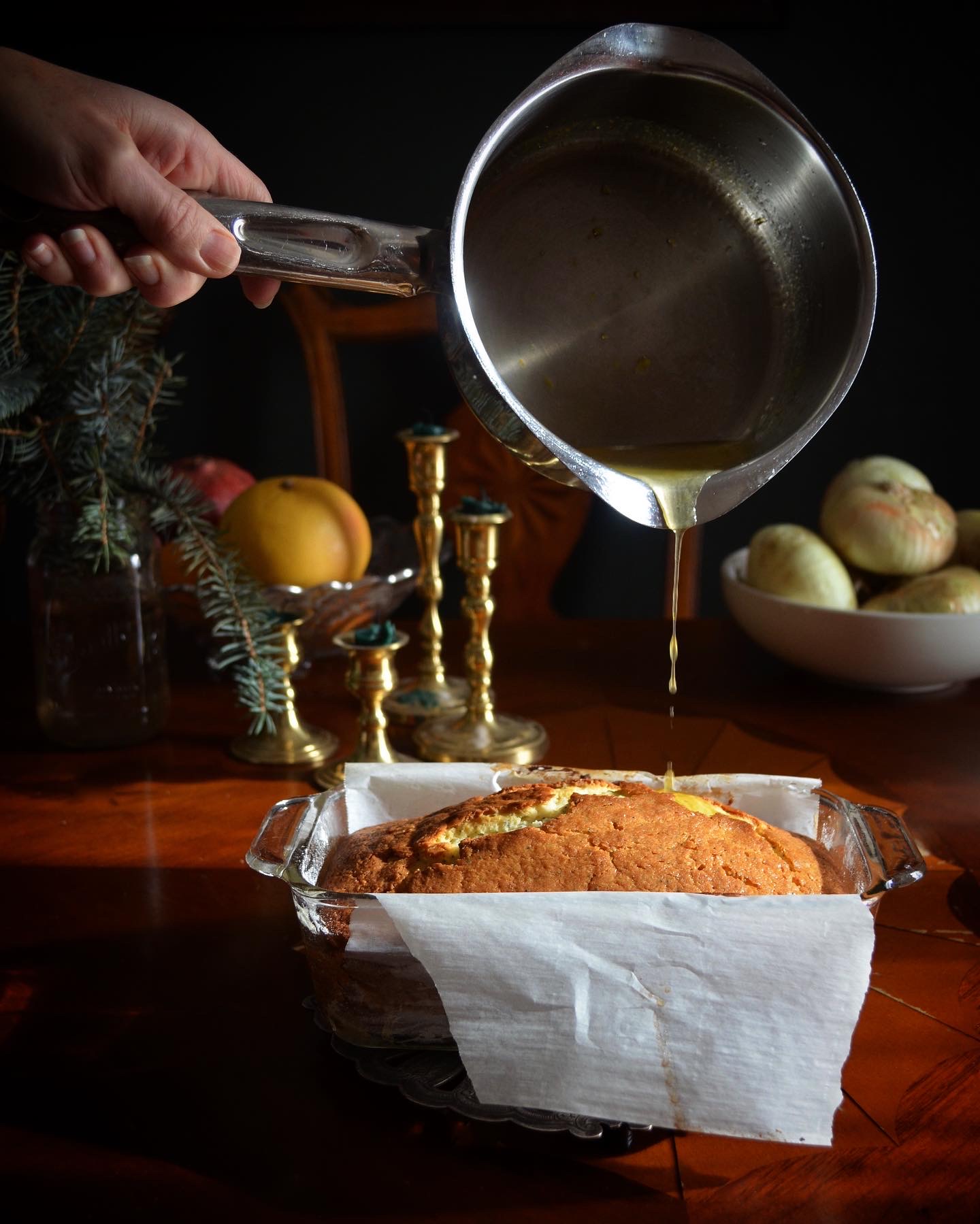 Pouring syrup over a baked cake in a glass dish, with a hand holding a saucepan, on a wooden table.