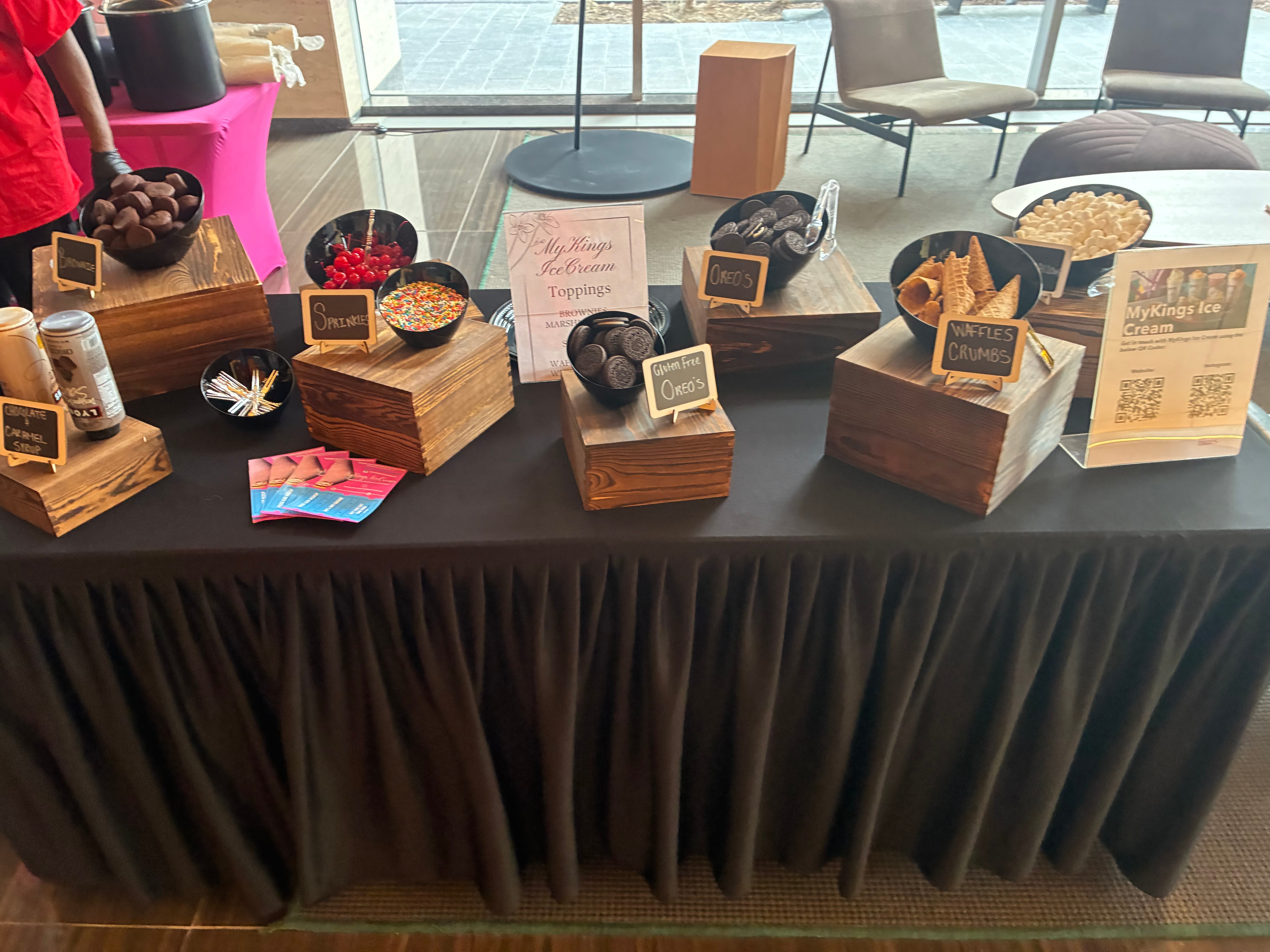 Display table with wooden boxes containing various small items, signs, and decorative objects, set in a bright indoor space.