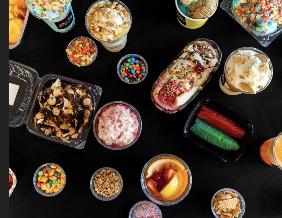 Assorted colorful candies, ice creams, and desserts on a black surface, with various toppings and decorations.