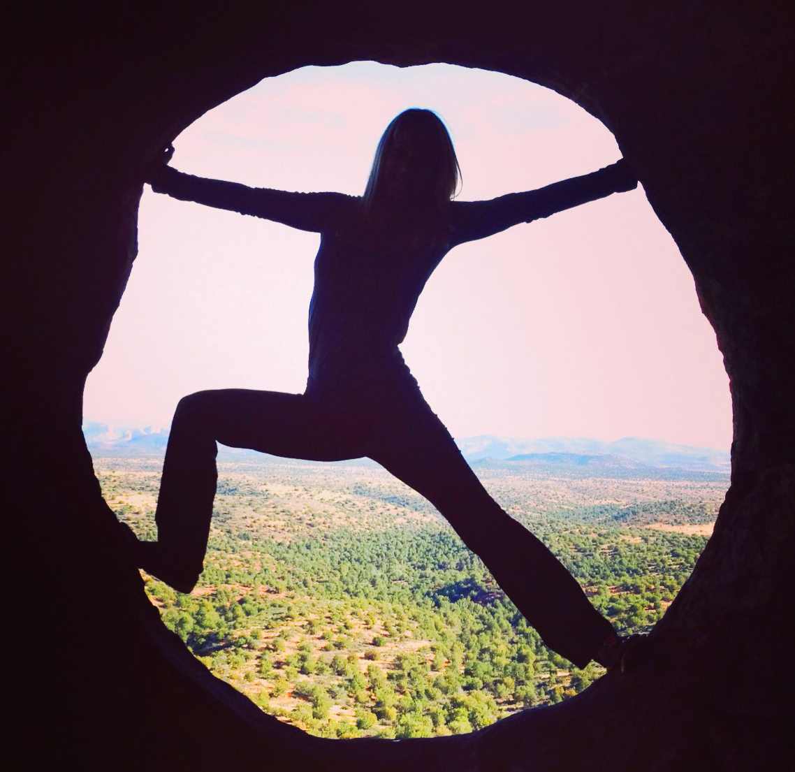 Silhouette of a person with arms and legs outstretched, standing in a circular opening with a landscape view behind.