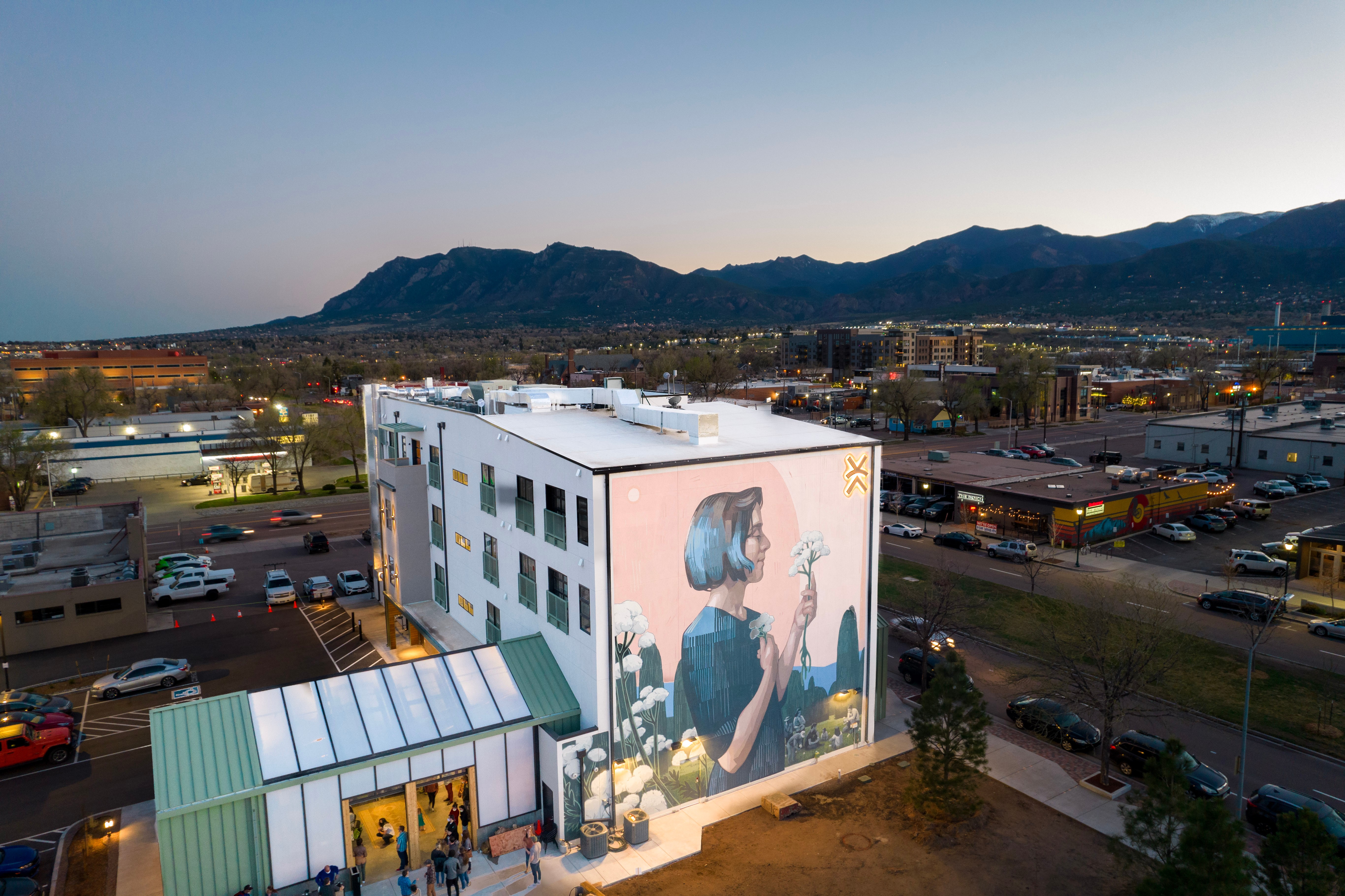 Building with a large mural of a girl holding a flower, parking lot, and mountains in the background.