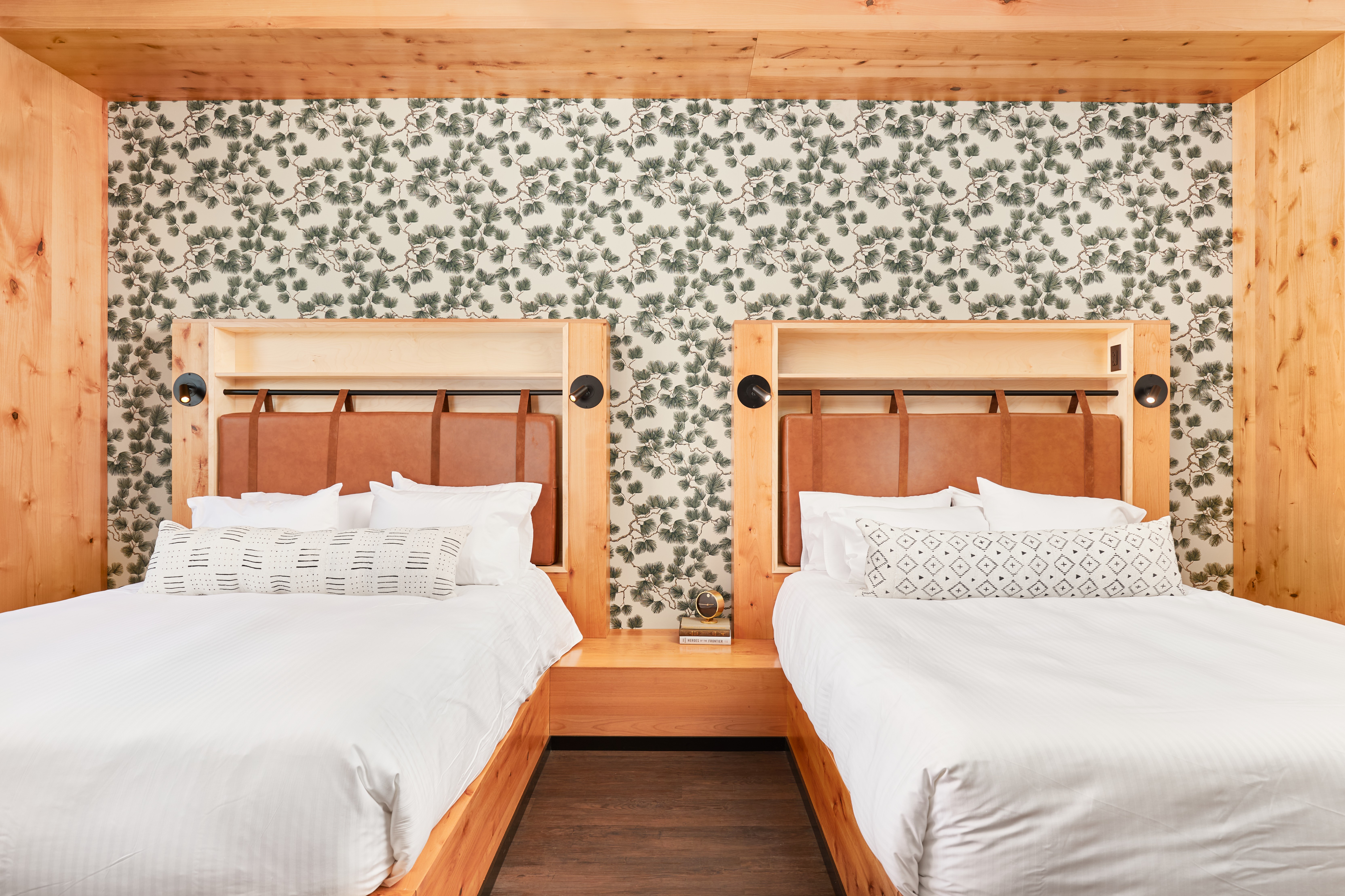 Two beds with wooden headboards and white bedding, against a floral patterned wall with wooden framing at the top and sides.